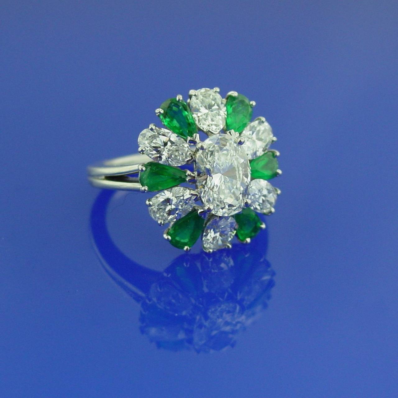 A classic Oscar Heyman emerald and diamond ring featuring a center oval shaped diamond surrounded by pear shaped emeralds and oval diamonds, mounted in platinum. The ring is set with approximately 2.50 carats of diamonds and approximately .90 carats