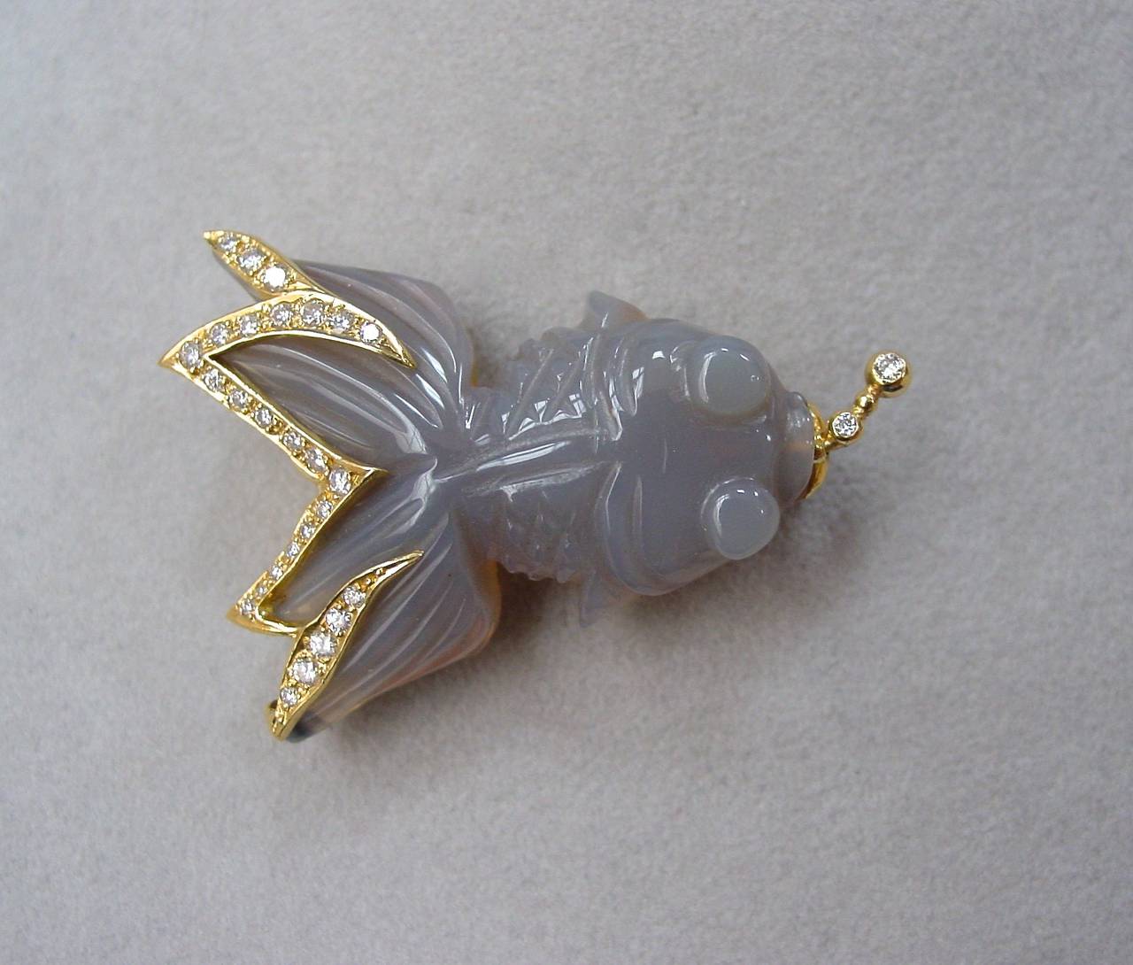A carved chalcedony, diamond and 18 karat yellow gold stylized koi brooch. Approximate total carat weight of.80 carats.