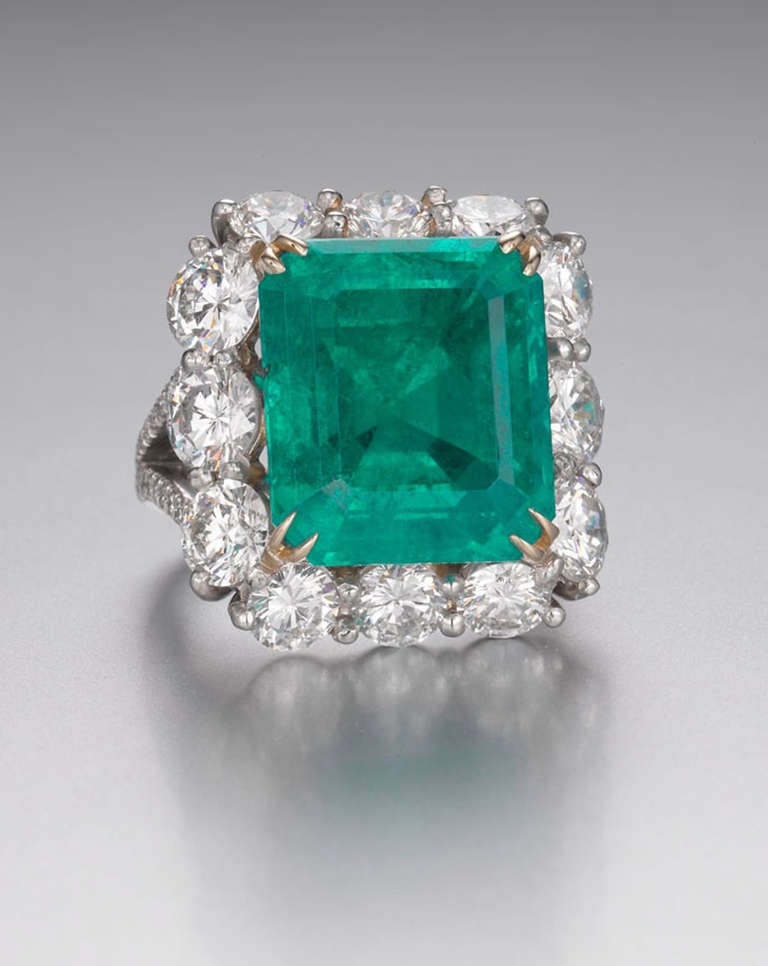 An emerald and diamond ring mounted in platinum and 18 karat yellow gold. The ring features a center emerald weighing 16.12 carats surrounded by twelve round brilliant cut diamonds, G-H in color, VS in clarity with a diamond pave mounting. Total