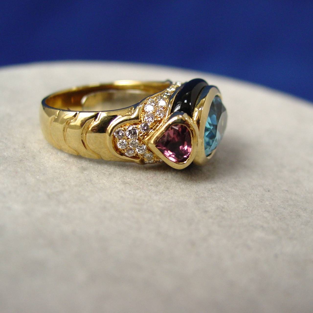 A Marina B Blue Topaz, Tourmaline, Onyx and Diamond Ring. The ring is set with a center oval shaped blue topaz, flanked by two heart shaped pink tourmalines and accented by onyx and round cut diamonds weighing approximately .50 carats. Signed Marina