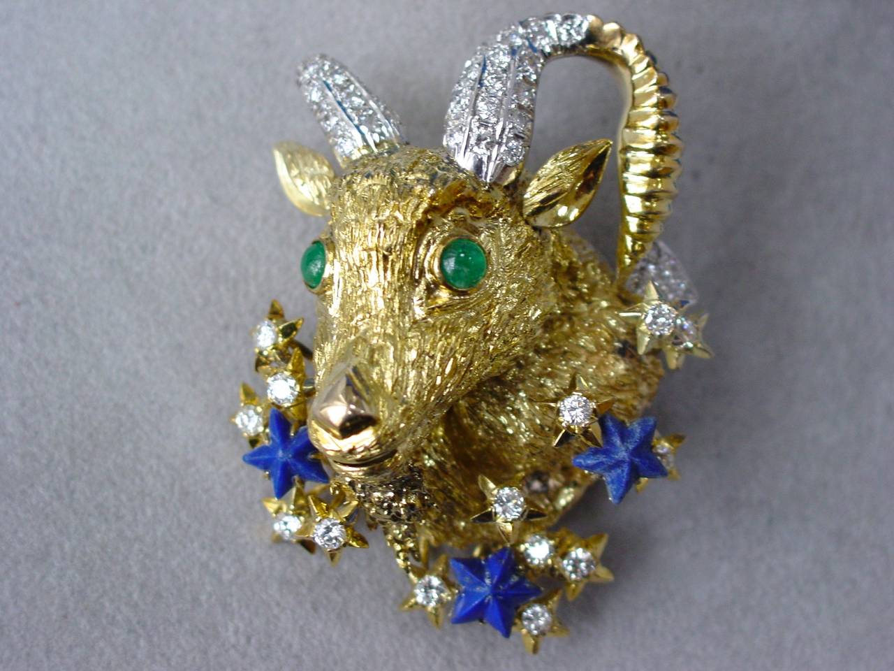 A wonderful and celestial Capricorn brooch set with emerald eyes, and decorated by carved lapis stars and round cut diamond detailing weighing approximately 2.70 carats. Mounted in 14 karat yellow and white gold with pendant attachment. Of probable