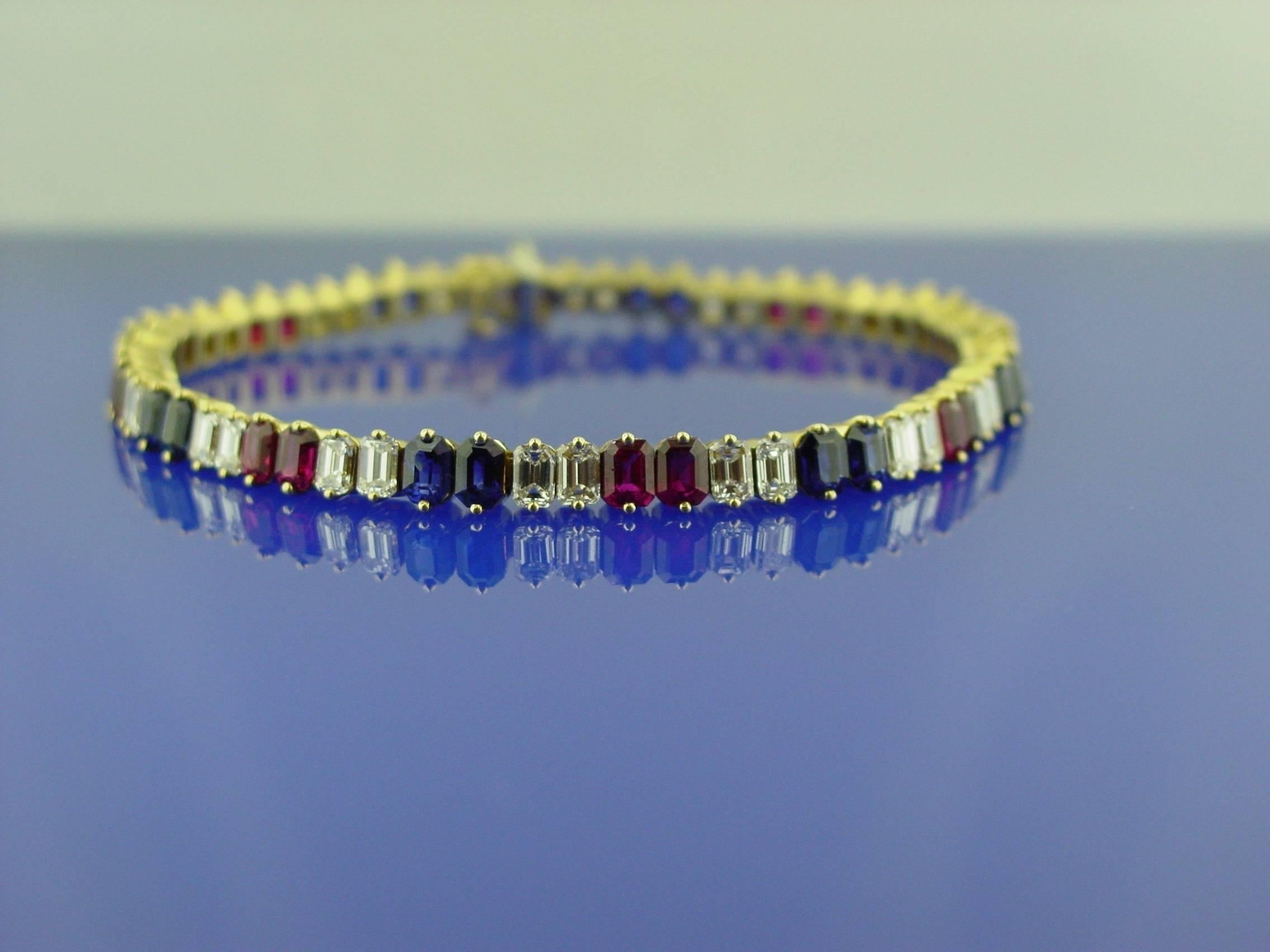 A beautifully bright ruby, diamond and sapphire line bracelet mounted in 18 karat yellow gold. The bracelet is set with thirty-two emerald cut diamonds weighing approximately 5.15 carats and approximately 6.65 carats each of emerald cut rubies and