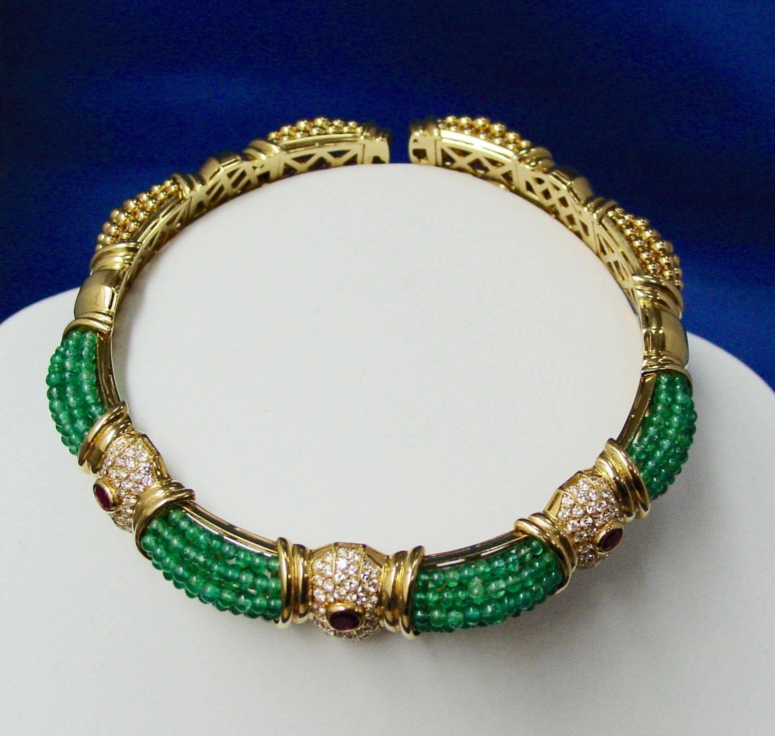 This lovely choker is a lively combination of  18 karat yellow gold and emerald beads highlighted by three sections each comprising an oval cut ruby surrounded by round brilliant diamonds, all mounted in 18 karat yellow gold.  The choker features