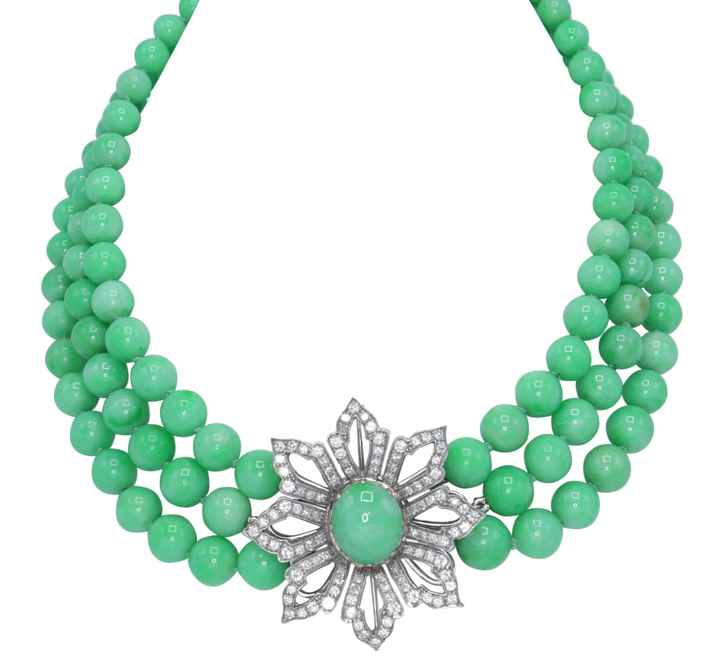A graduated natural jadeite and diamond necklace composed of three strands of jadeite measuring 5.5 to 10.2 mm., the detachable clasp designed as a flowerhead set in the center with a cabochon jadeite section, with petals set with round diamonds