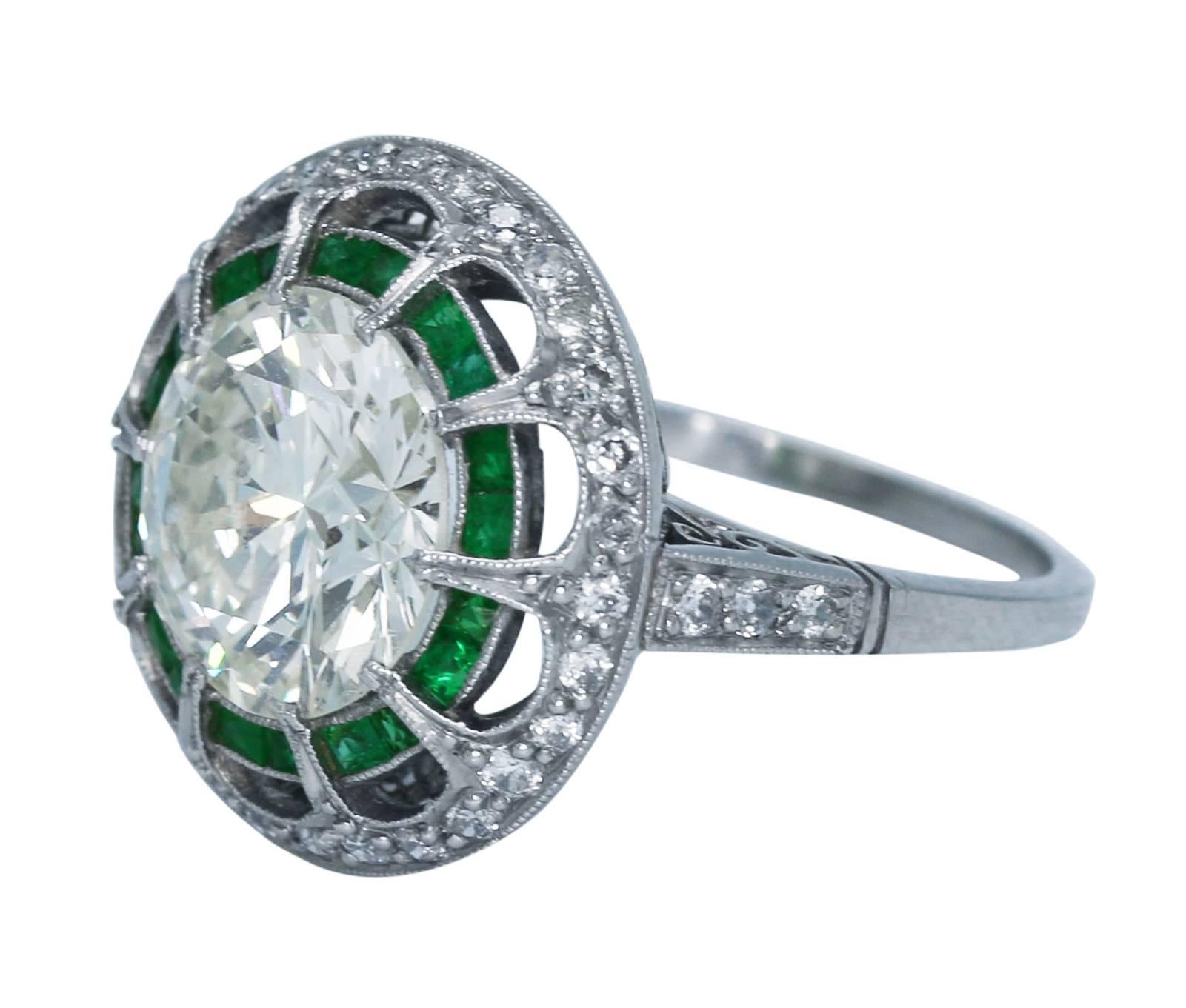 An Art Deco Style ring set in the center with a round diamond weighing 4.09 carats, within a frame of calibré-cut emeralds weighing approximately 0.80 carat, and diamonds weighing approximately 0.65 carat, size 6 3/4, mounted in platinum, gross