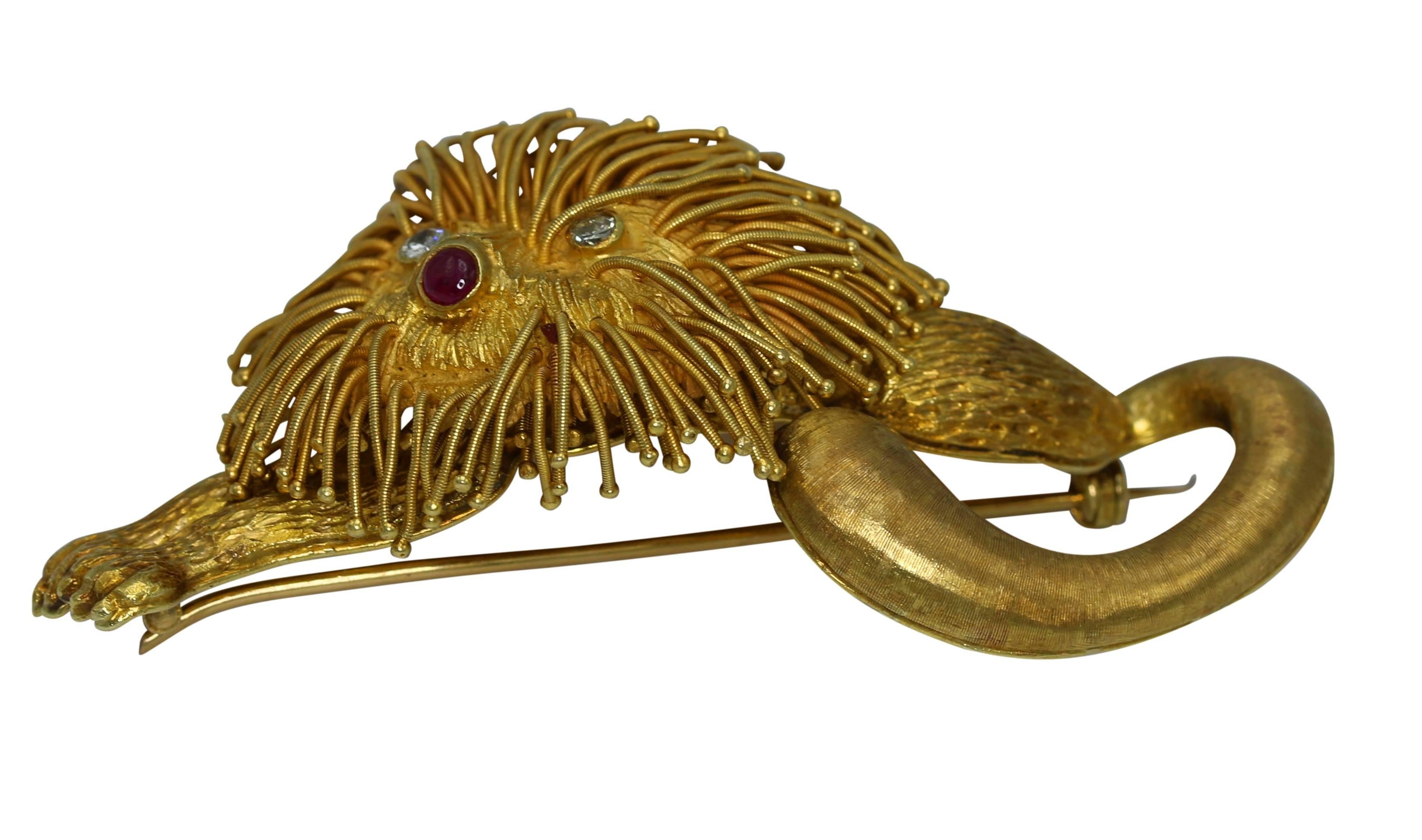 A regal lion brooch by Lalaounis, Greece, designed as a textured gold reclining lion with arms stretched and tail curled, the eyes set with round diamonds weighing approximately 0.20 carat, the nose set with a cabochon ruby, mounted in 18 karat