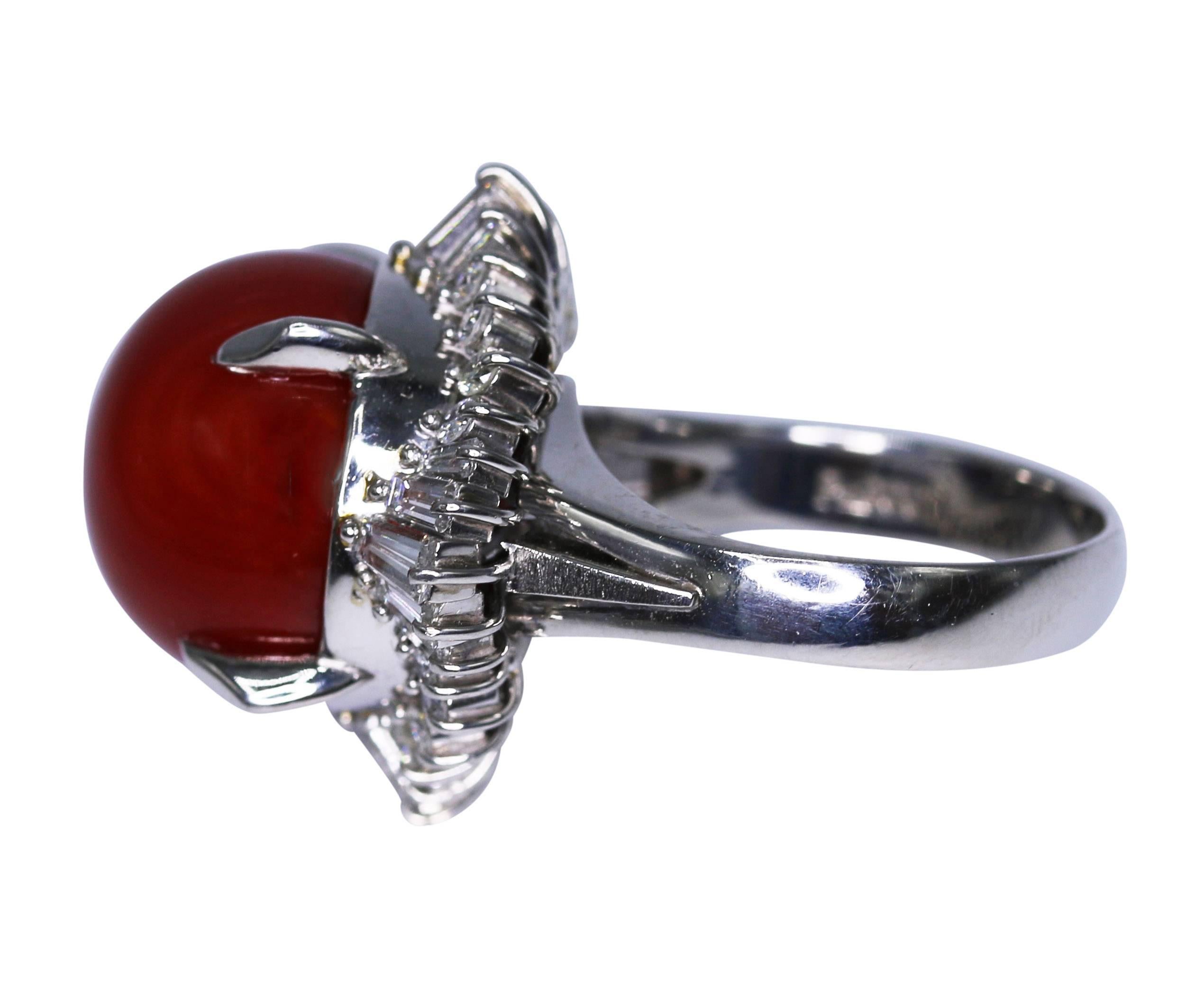 Platinum, Japanese Aka coral and diamond ring, set in the center with a round deep red cabochon coral, framed by diamonds weighing approximately 1.15 carats, gross weight 14.9 grams, size 5, measuring 1 1/4 by 7/8 by 7/8 inches. The coral is of a