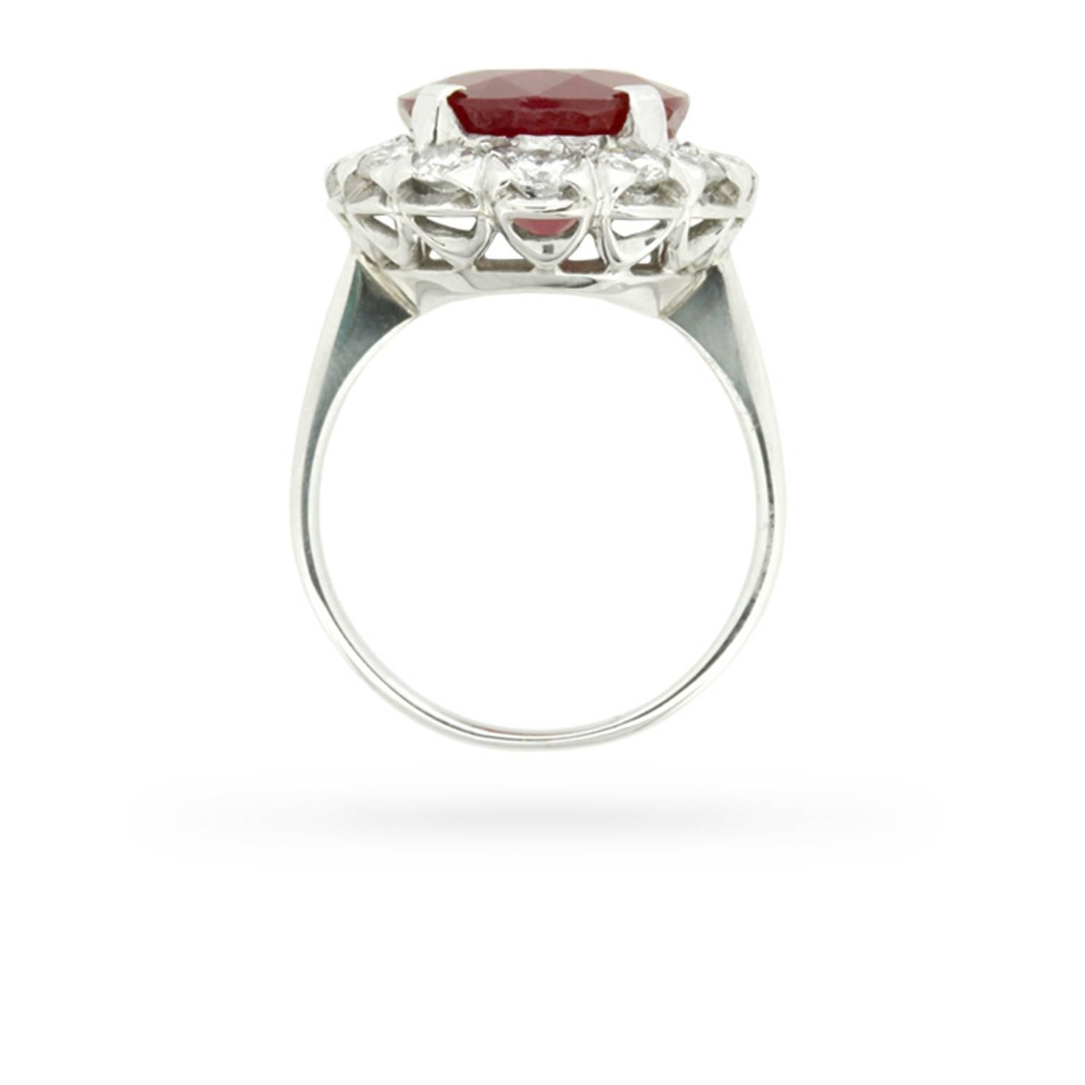 This stylish and sophisticated 1950s era ring is set to show off a tantalising 7.91 carat oval-shaped faceted ruby amid a halo of twinkling high-quality round brilliant cut diamonds totalling 1.12 carats, all set within a decorative openwork gallery