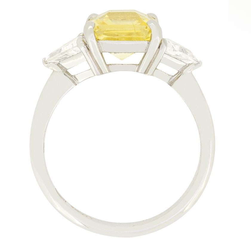 Uno splendido zaffiro giallo è affiancato da diamanti taglio trilione in questo anello trilogy vintage. Lo zaffiro giallo centrale è una pietra naturale non riscaldata del peso di 2,27 carati. La pietra ha un taglio asscher ed è completamente