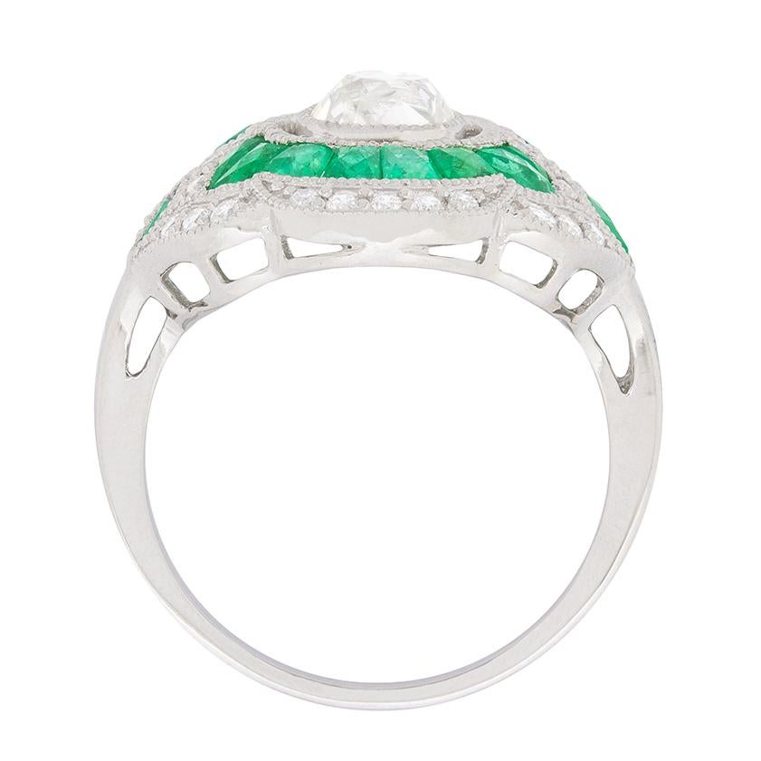 This beautiful ring features a centre diamond weighing 0.80 carat. It has been estimated as H in colour and SI in clarity. It is haloed by wonderfully green emeralds, all hand cut to fit the design of the floral cluster ring. They total 1.50 carats