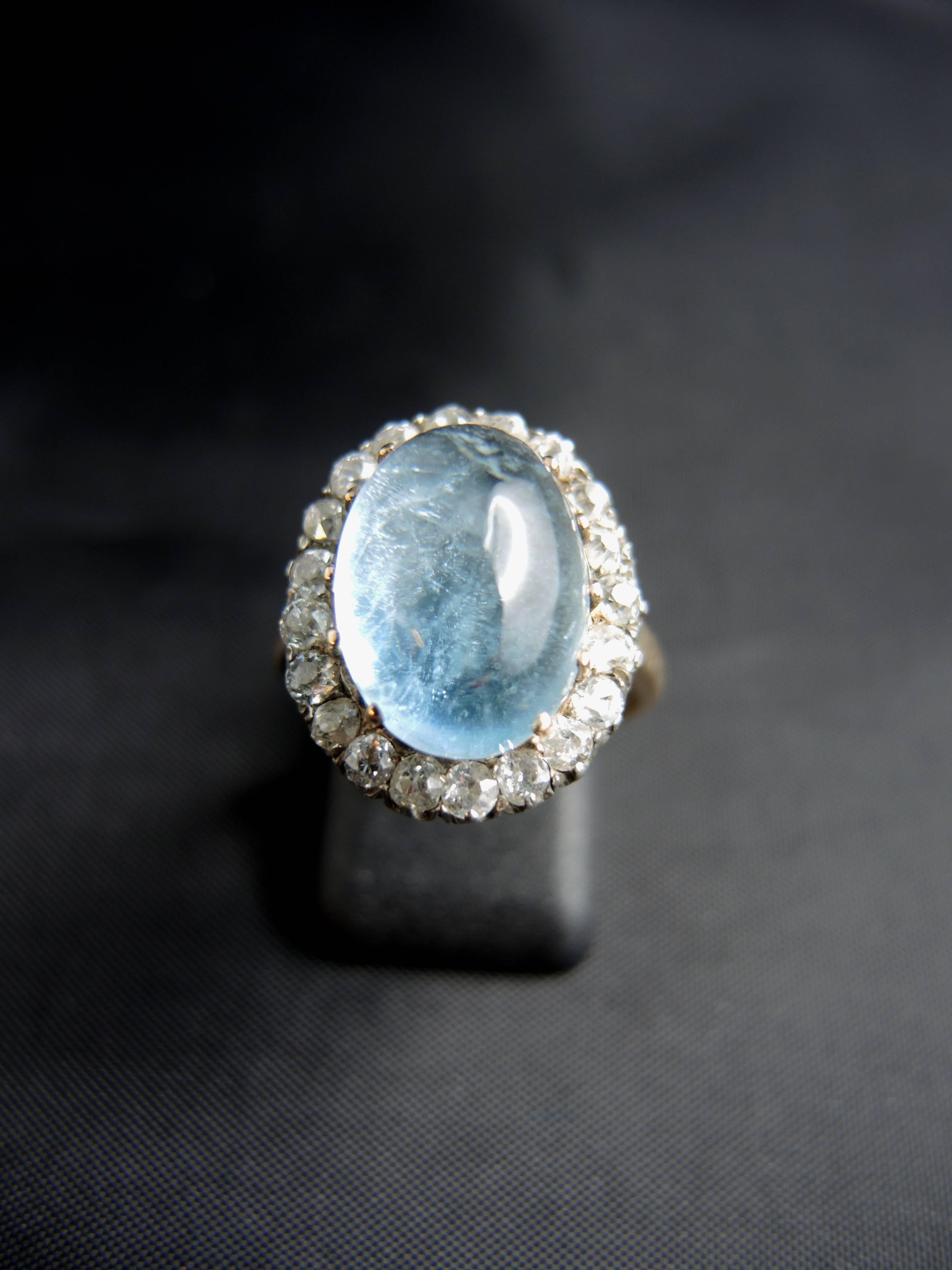 14kt gold and silver cluster ring (quality mark: scallop and swan) set with a superb 12,00 cts cabochon of aquamarine, surrounded with old cut diamonds, total weight estimated around 0,80ct.

Work from the 19th century.

Weight: 4,60g
Ring size: 51