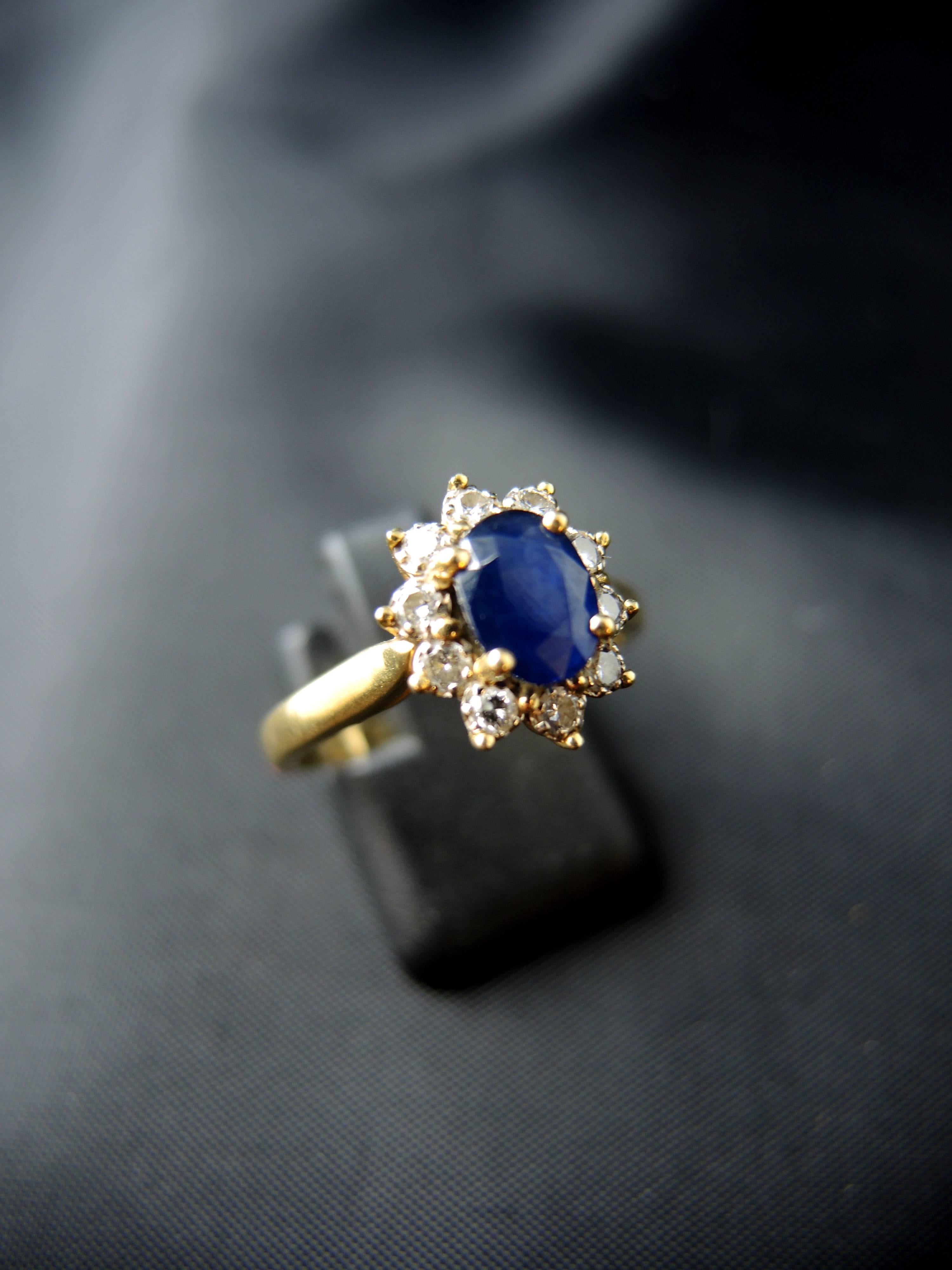 Yellow gold cluster ring (quality mark: head of eagle) set with a central oval sapphire, weight estimated  around 1,00 Ct, surrounded with modern brillant cut diamonds, which total weight is estimated around 0,40 Ct.

French work, circa