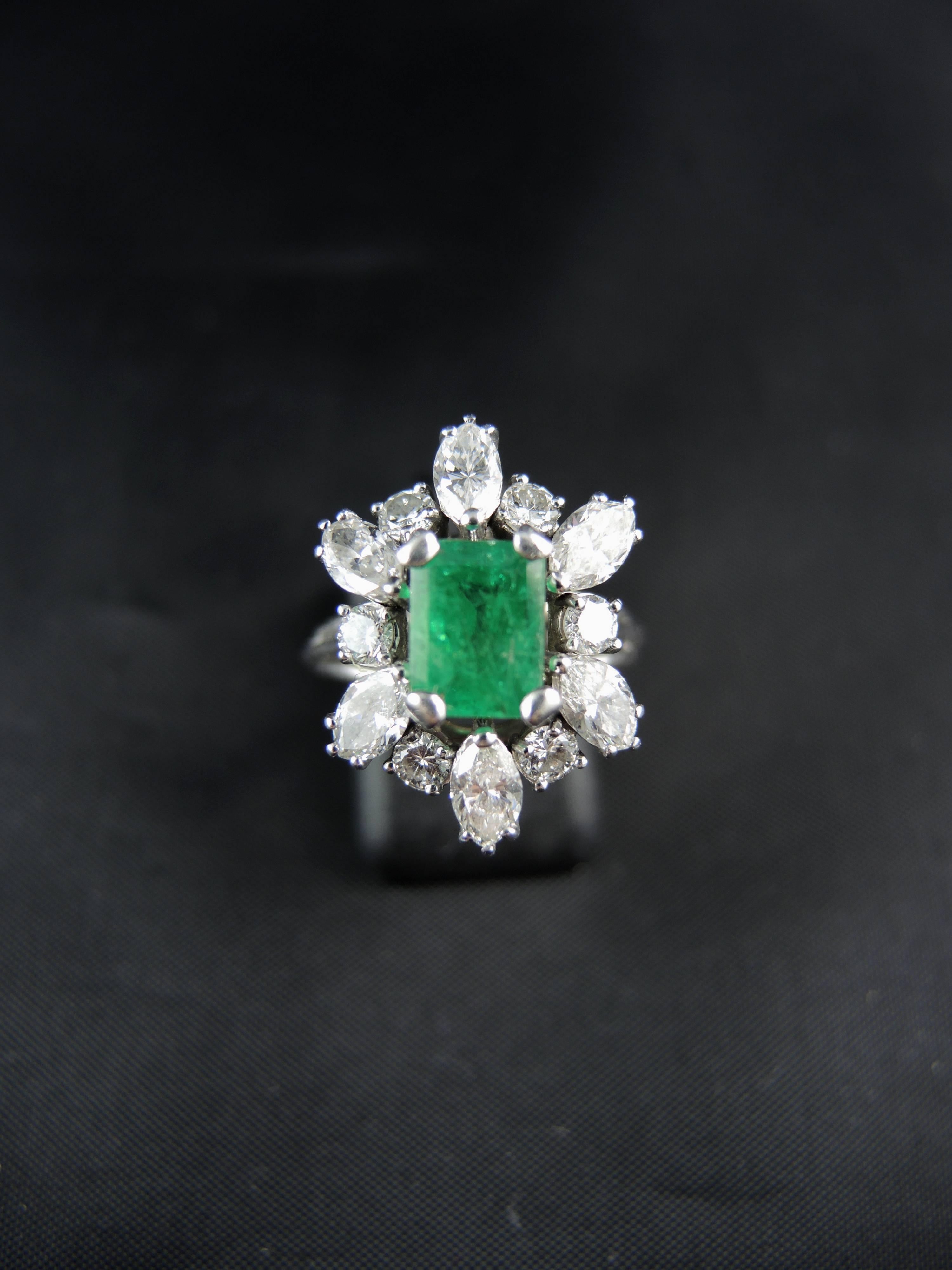 18 Kt white gold and platinium cluster ring (quality mark: head of eagle and dog) set with a central emerald cut emerald, weight estimated around 1,45 Cts, surrounded with modern brilliant  and navette cut diamonds, which total weight is estimated