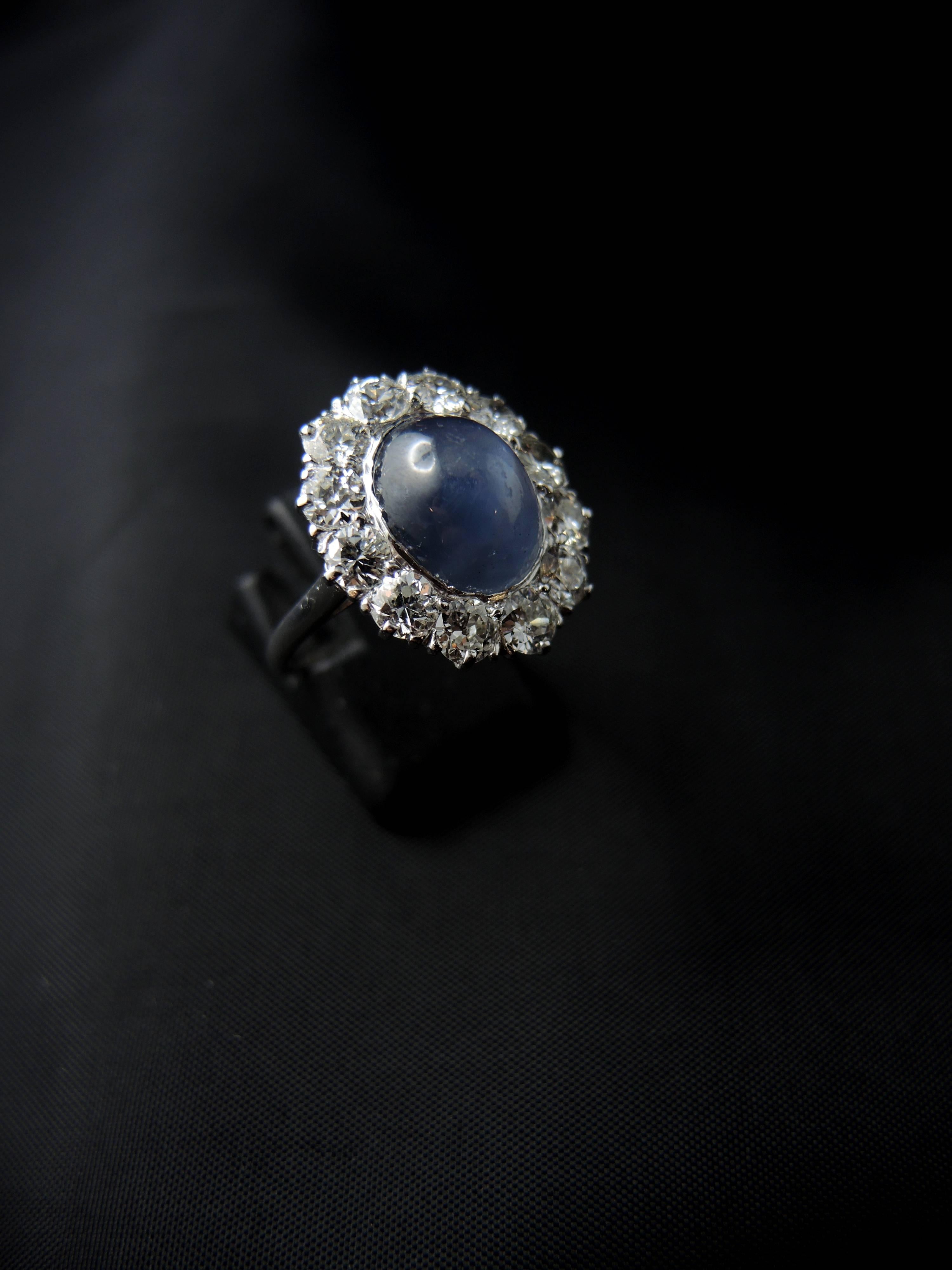 White gold cluster ring (quality mark: head of eagle) set with a central oval star (6 rays quite easily visible) sapphire, weight estimated around 10.00 Cts, surrounded with old cut diamonds, which total weight is estimated around 2,35 Cts, color