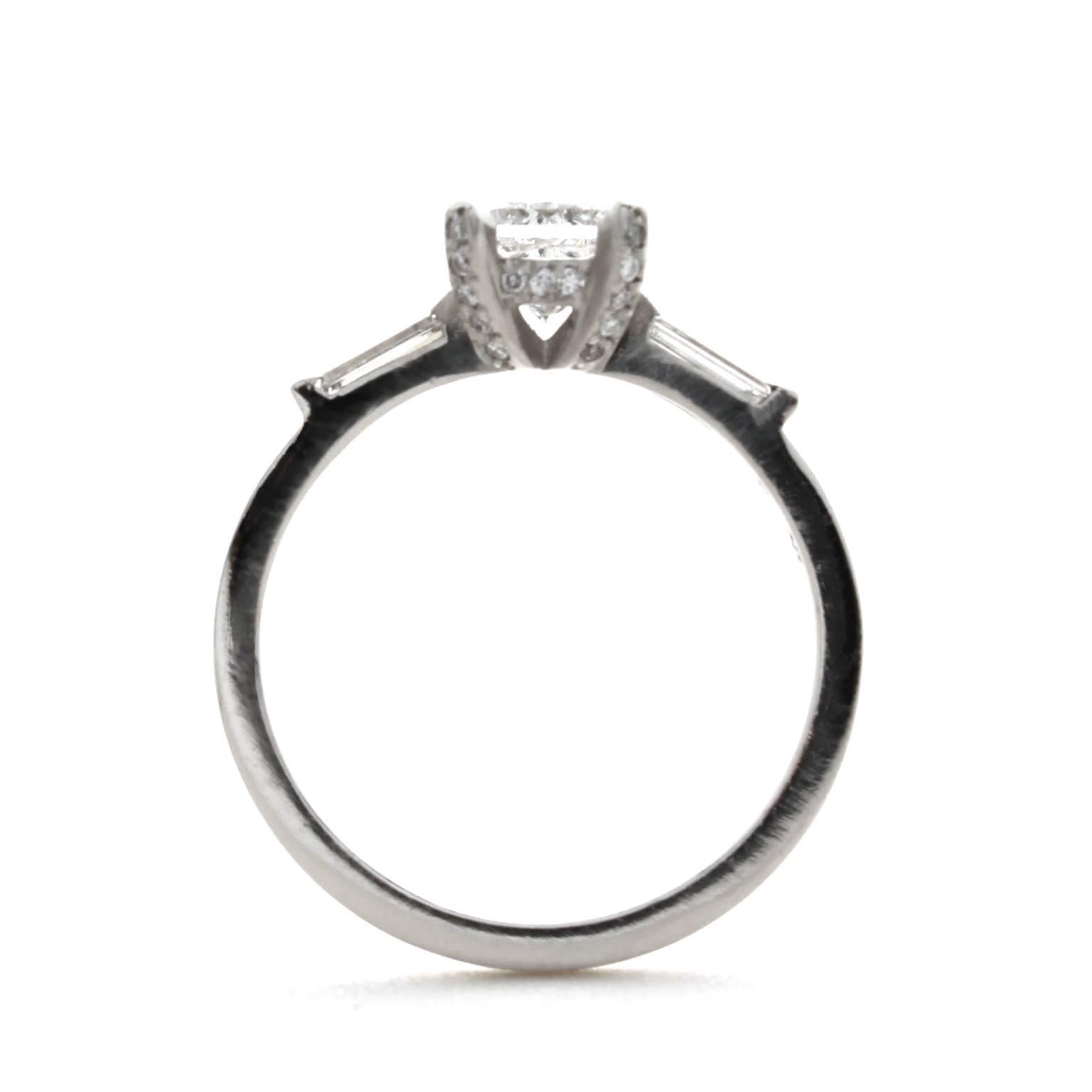 This modern three stone diamond ring features a 0.78ct princess cut diamond with VS2 clarity and I color. It is accented with baguette diamonds and pave set round diamonds on the prongs. The total weight of the baguette diamonds is 0.22ct, with VS