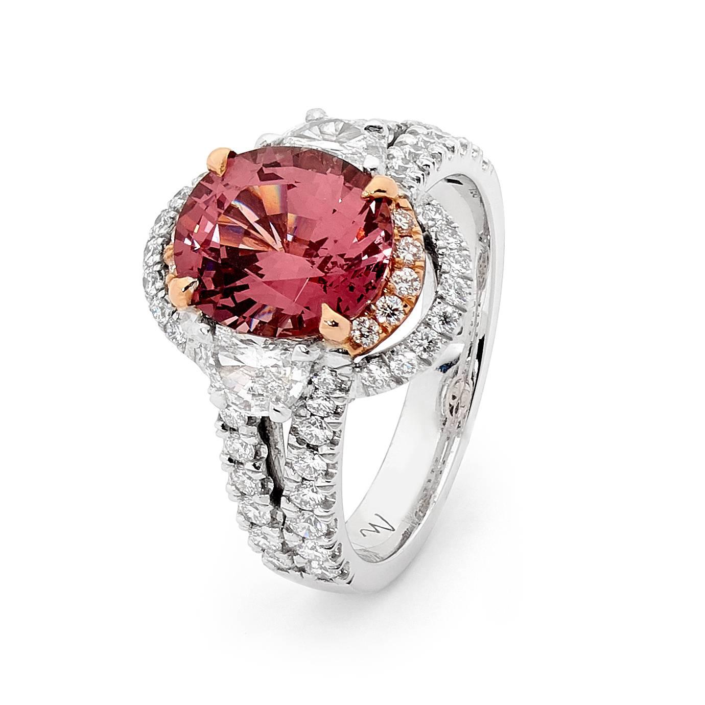 Two tone 18ct white gold and rose gold halo dress ring set with an oval cut Malaya garnet weighing 3.54 ct and a pair of half moon diamonds on the shoulder that total 0.51 ct and are of F colour and VS+ clarity. The double halo consists of 68 round