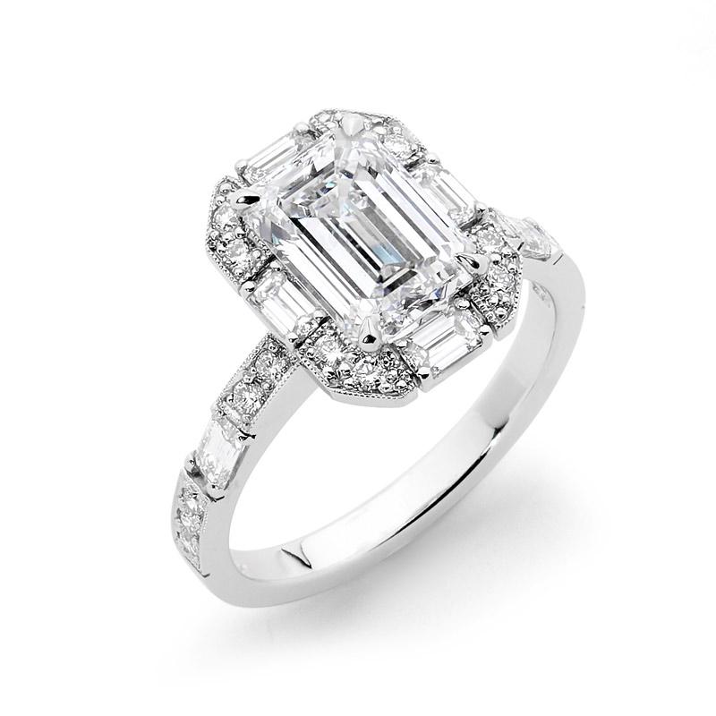 Platinum Art Deco Inspired Diamond Engagement ring set with a 2.46ct Emerald Cut Diamond. Complimented with milgrain detailing, Emerald Cut and Brilliant Cut Diamonds in the halo and band. 