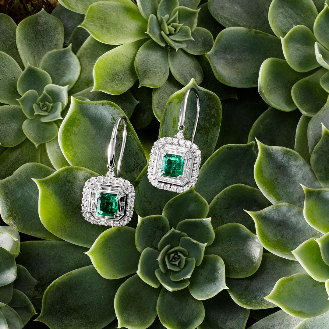 Crafted with 18ct White Gold, these striking Matthew Ely Art Deco inspired drop Earrings showcase 2 emerald cut Emeralds (total weight 1.3ct) enclosed in Round Brilliant Cut and Baguette Diamonds (total weight 1.314ct).  

Made to order - some