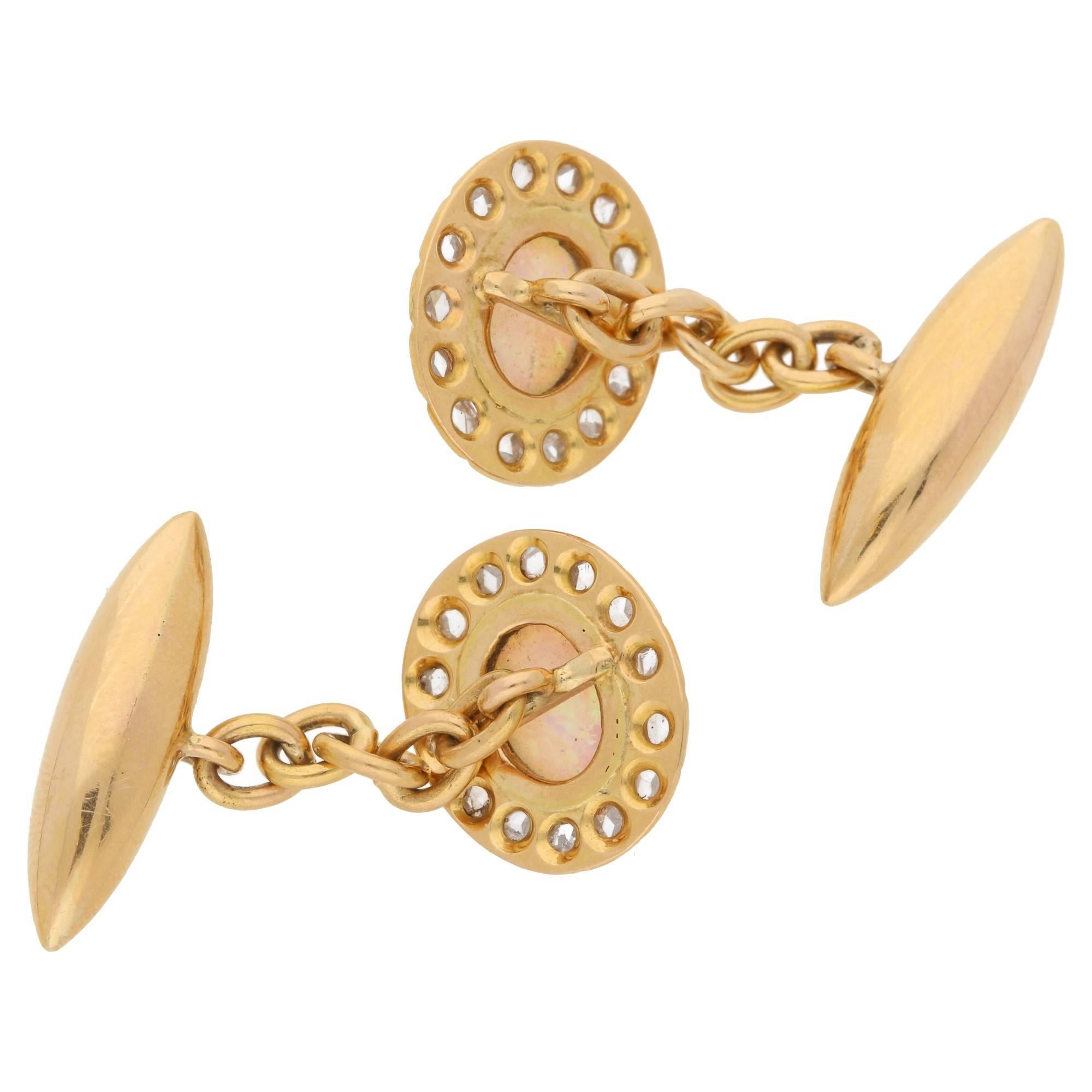 A pair of Victorian opal and diamond 18ct yellow gold cufflinks. With a centrally set oval cabochon opal mille grain set in 18ct yellow gold surrounded by a border of fourteen pinch set rose cut diamonds. On a classic five link chain and torpedo