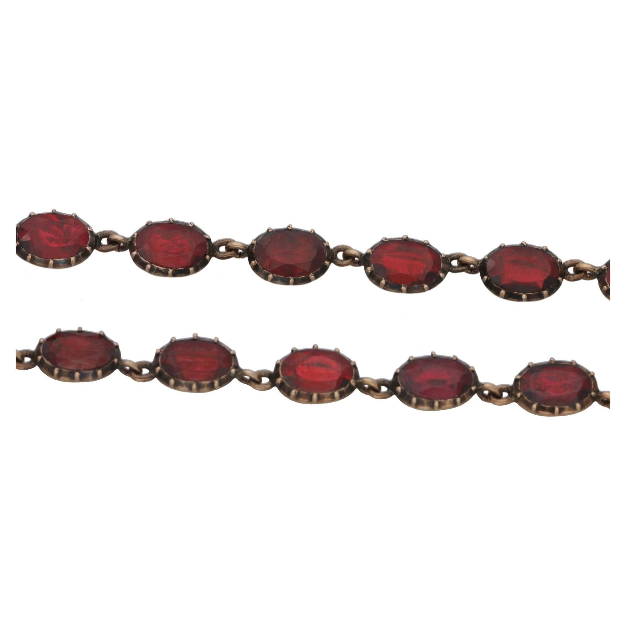 A vibrant Victorian riviere garnet necklace foil back set in 9ct yellow gold. Comprising of thirty five foil backed oval faceted garnets closed backed set in 9ct yellow gold. With an invisible tongue in groove clasp hidden behind one of the garnets.