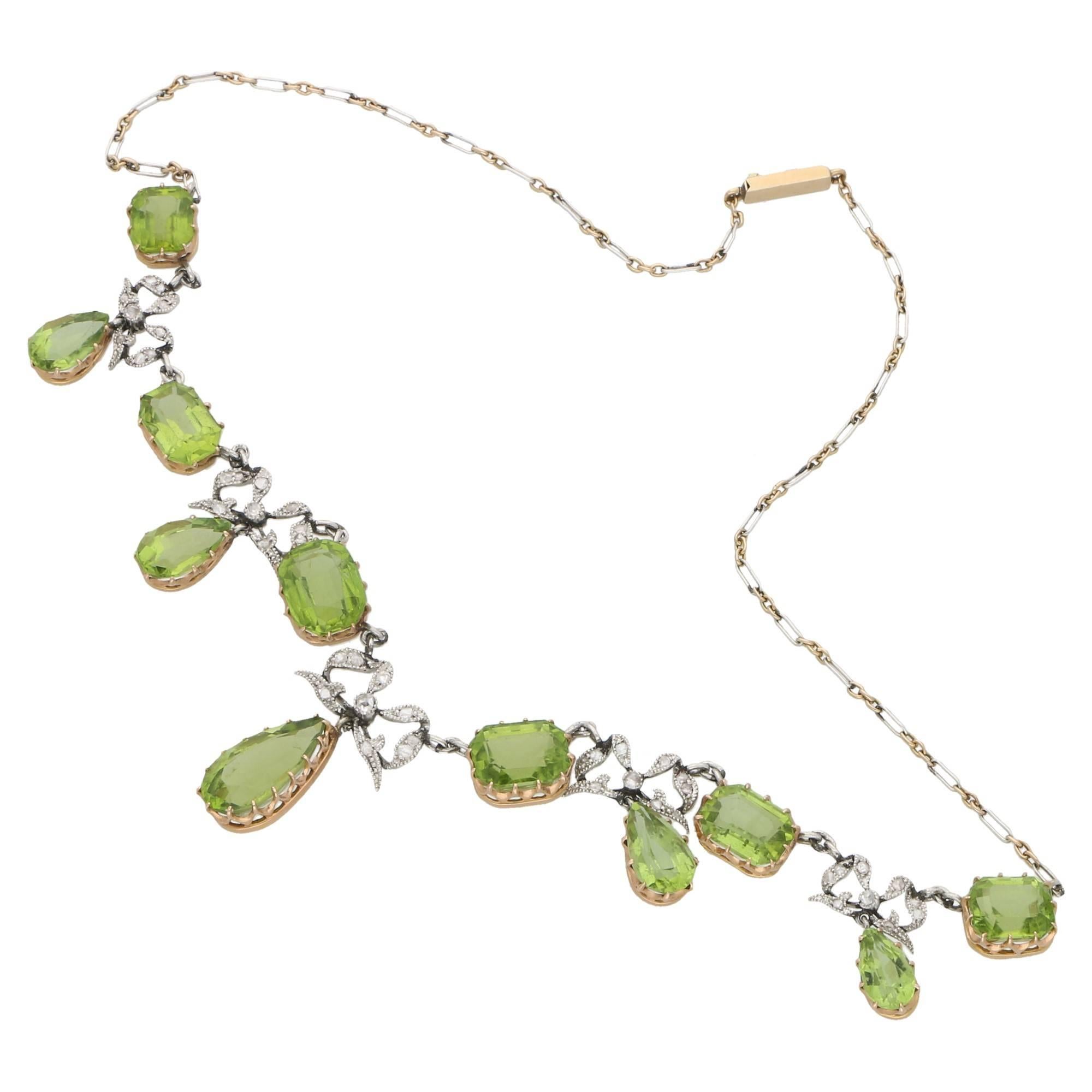 An Edwardian peridot and diamond necklace, set in platinum, backed in gold. With six step-cut peridots claw set in 18ct yellow gold aligned along the chain. Then a further five pear-cut claw set peridots suspended from diamond set platinum bows.