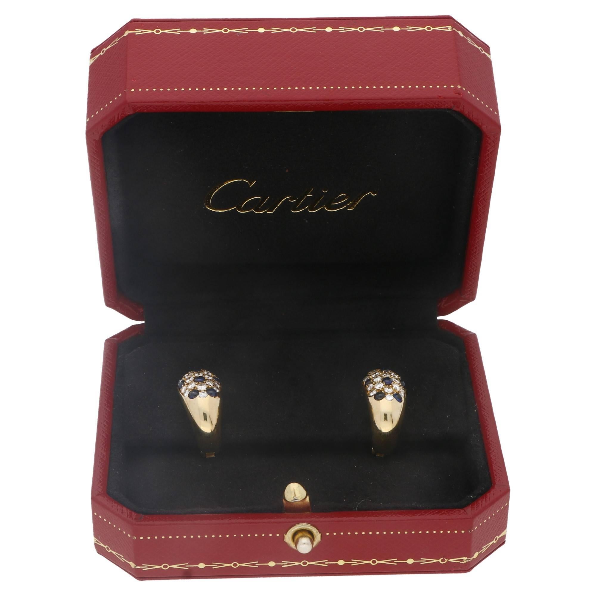 Diamond and blue sapphire set 18K yellow gold earrings by Cartier. These are set with round brilliant cut diamonds and striking blue sapphire cabochons. Hallmarked: Cartier, 1989. On post and clip fittings