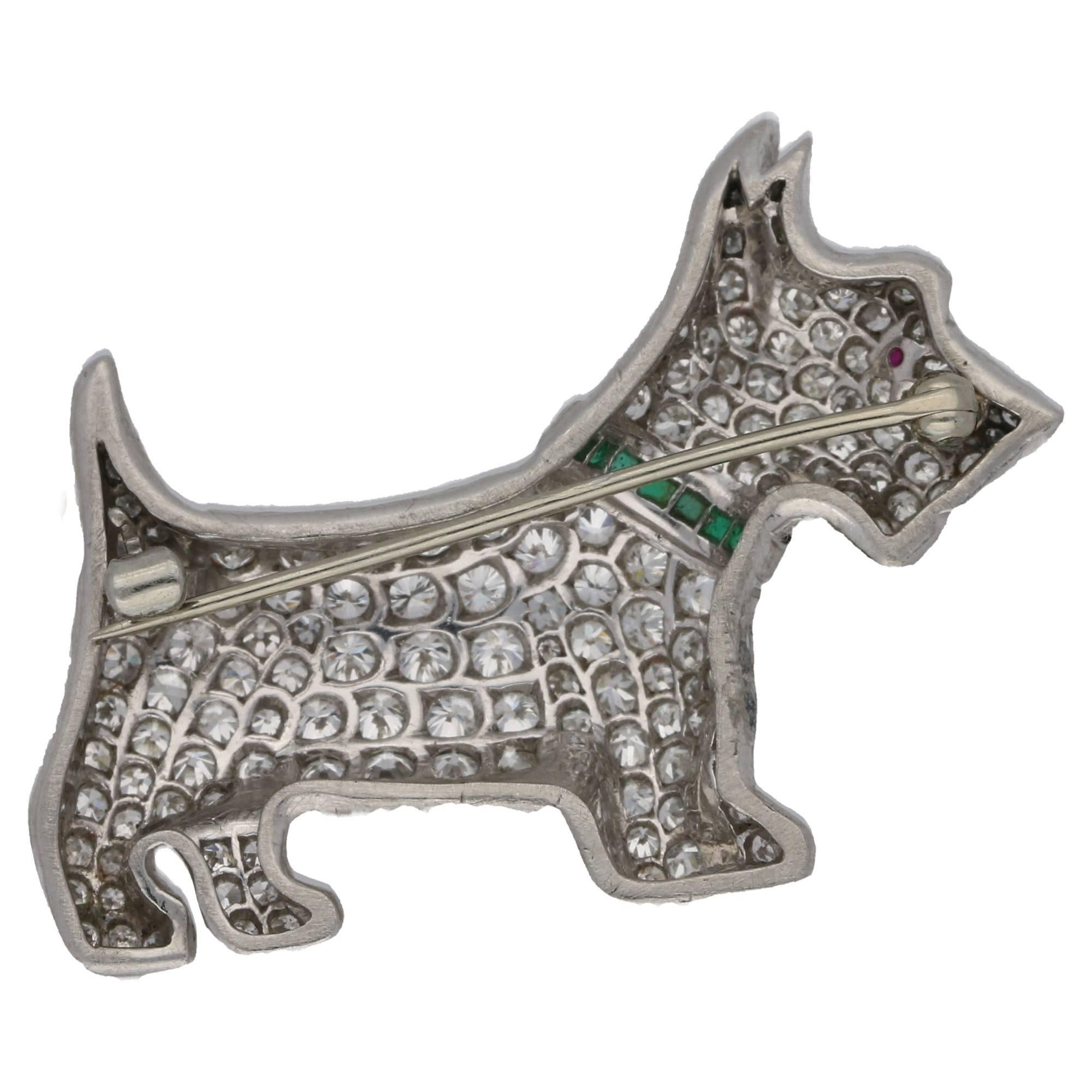 A charming Scottie dog diamond, emerald and ruby brooch in platinum. This lovely brooch is beautifully hand crafted and  pavé set throughout with over 120 diamonds which sparkle incredibly in the evening. It also has a lovely emerald collar with