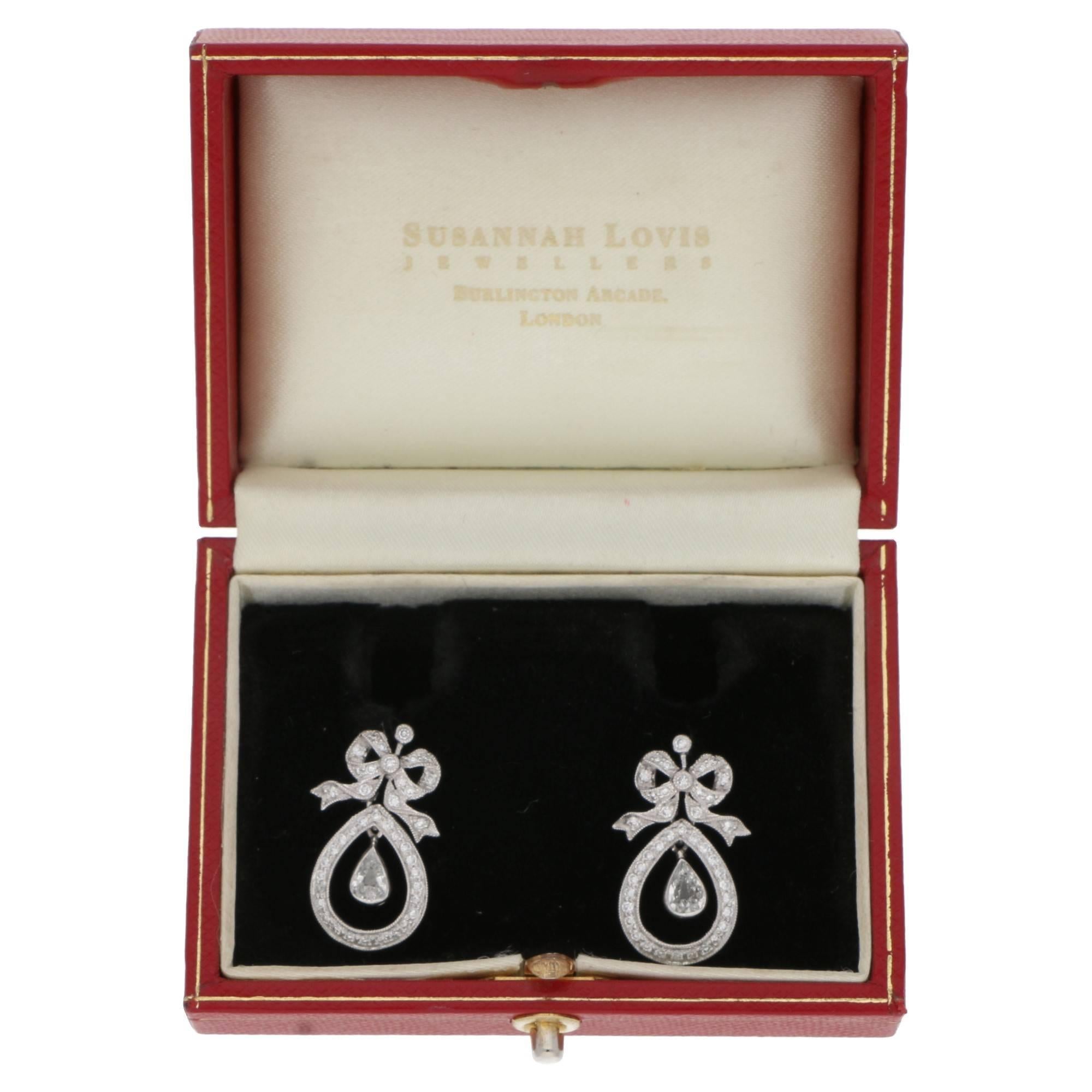 A fantastic pair of 18ct white gold Edwardian style diamond drop earrings. Each earring has a coture bow detail top set with round brilliant cut diamonds in a channel and grain setting with mille grain edges. Suspended from the bow is an articulated