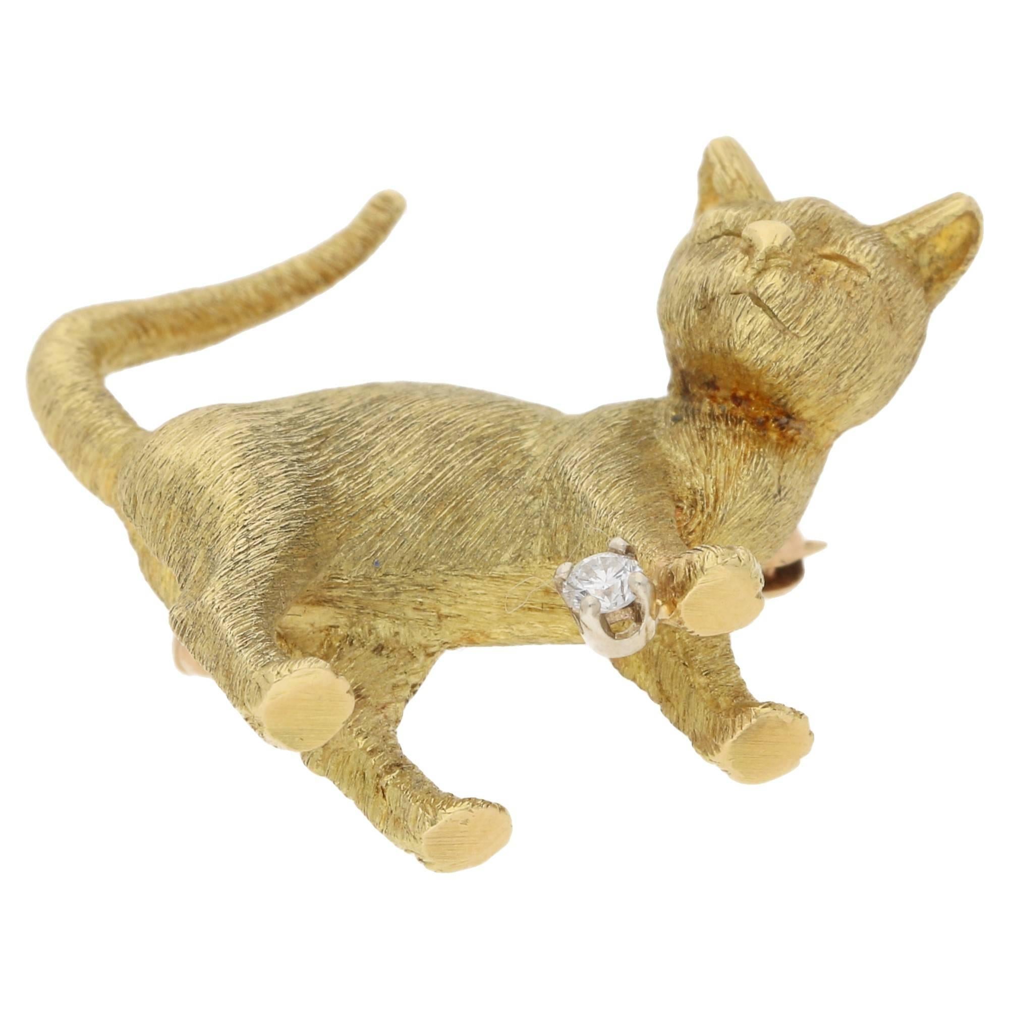 A whimsical 18ct yellow gold and diamond hand carved cat brooch. The hand tooled cat displays a florentine effect to the gold surface and is playing with a small round brilliant cut diamond four-claw set in platinum. Estimated diamond weight: 0.05.