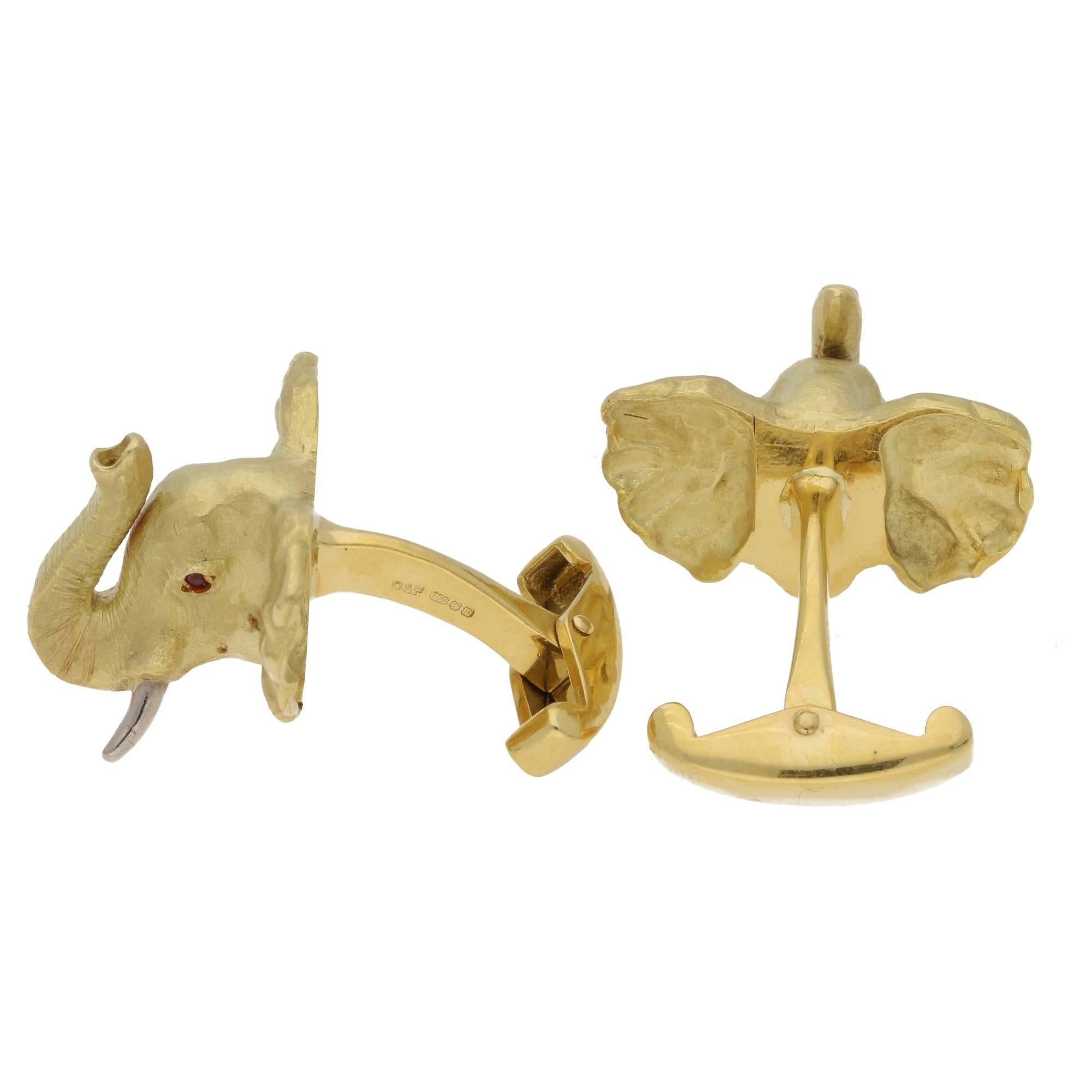 A pair of meticulously designed 18ct yellow gold elephant cufflinks. With an expressive hand crafted 18ct yellow gold skin texture enhanced with 18ct white gold tusks and round facted ruby eyes. One bar and swivel back fittings. Estimated total ruby