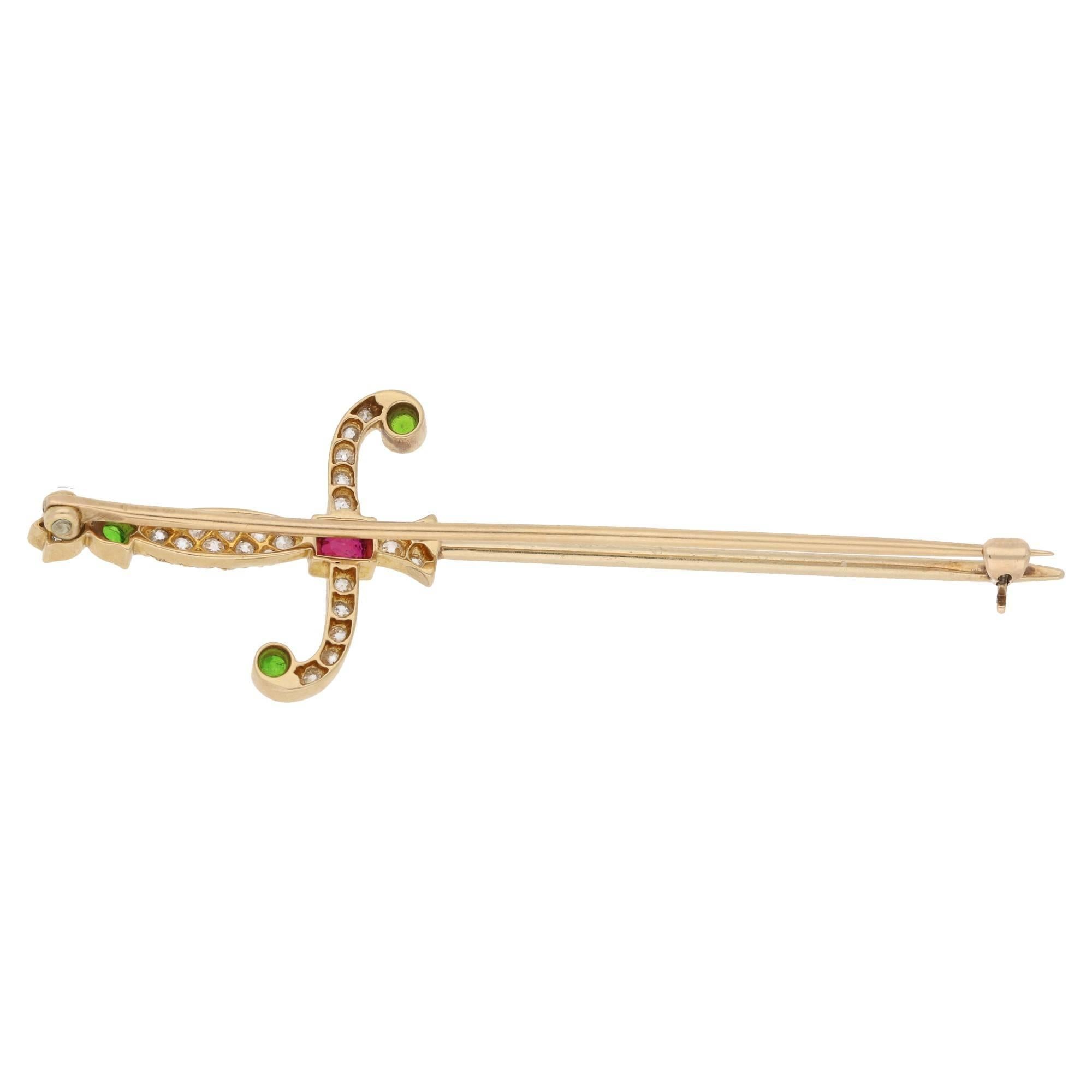 An 18ct yellow gold Edwardian rapier brooch set with diamonds, demantoid garnets and a Burmese ruby. The pommel is set with an Old European cut diamond the head is set with a demantoid garnet, the handle is set with Old European cut diamonds set to