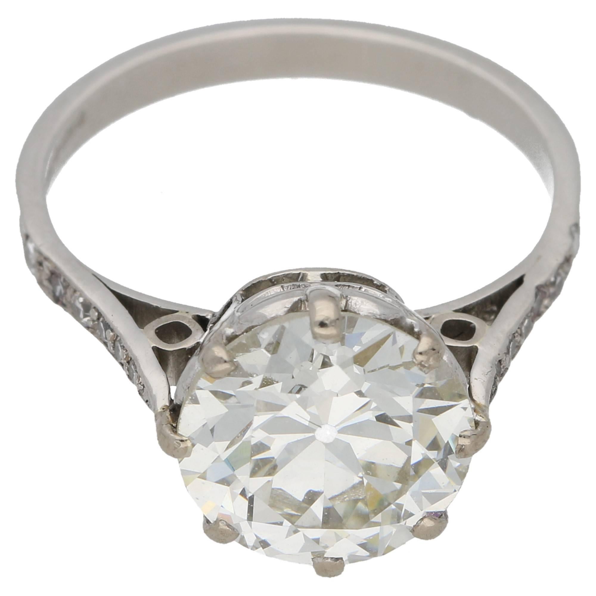An Edwardian platinum single stone diamond ring, featuring a 2.78ct L colour and VS1 clarity Old European cut diamond, set in an eight claw setting with scroll detailing on the sides and open daylight shoulders each featuring six grain set diamonds.