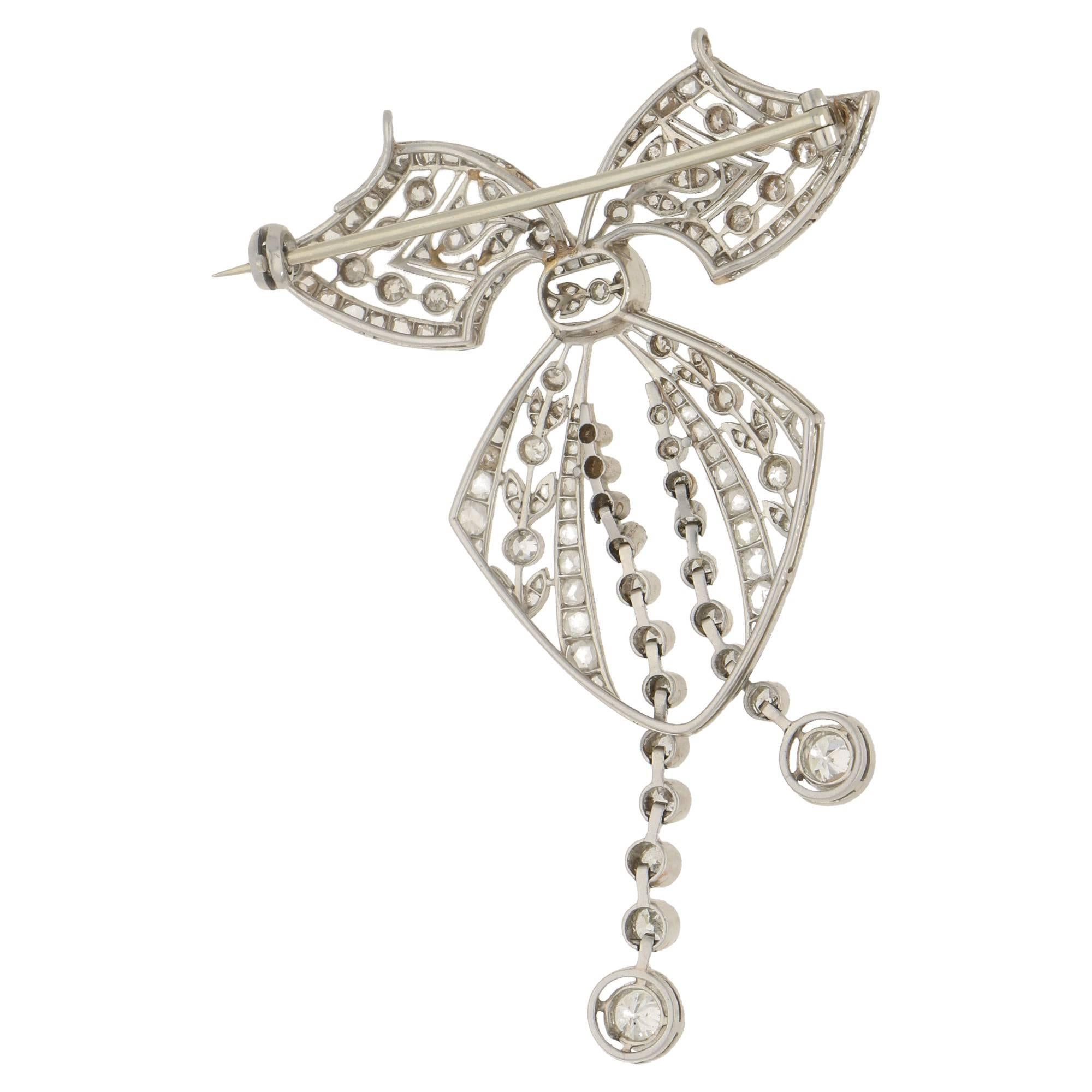 A diamond set negligee bow brooch. The early 20th century brooch is formed of fine hand pierced platinum openwork. The main body of the brooch is set with eight cut diamonds and the negligee motif is formed of a graduated line of eight cut and old