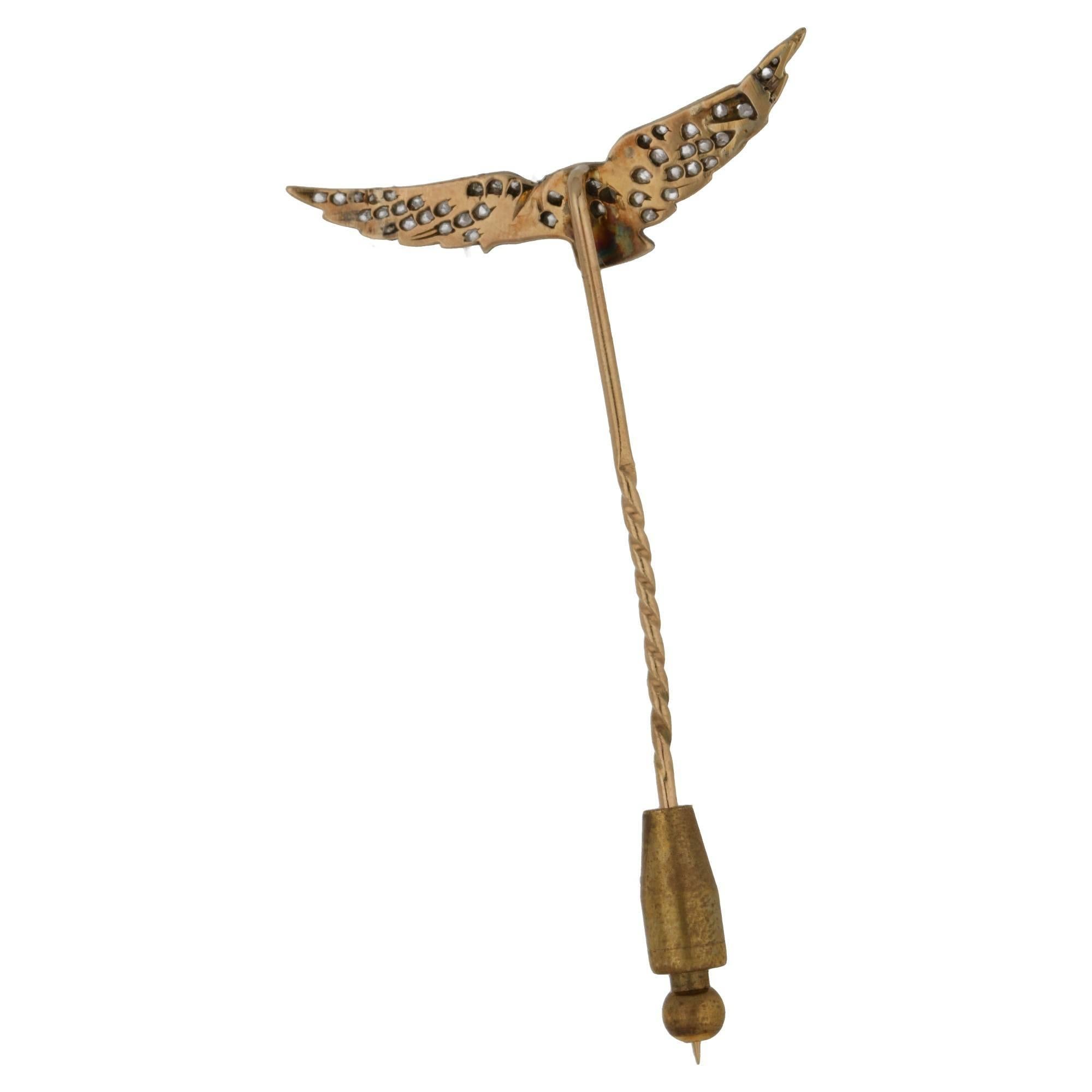 A fabulous diamond set eagle design stickpin. The white and yellow gold stick pin depicts an eagle in flight, it's body is fully adorned with eight-cut diamonds and a ruby for the eye. With stopper for security, in gold.