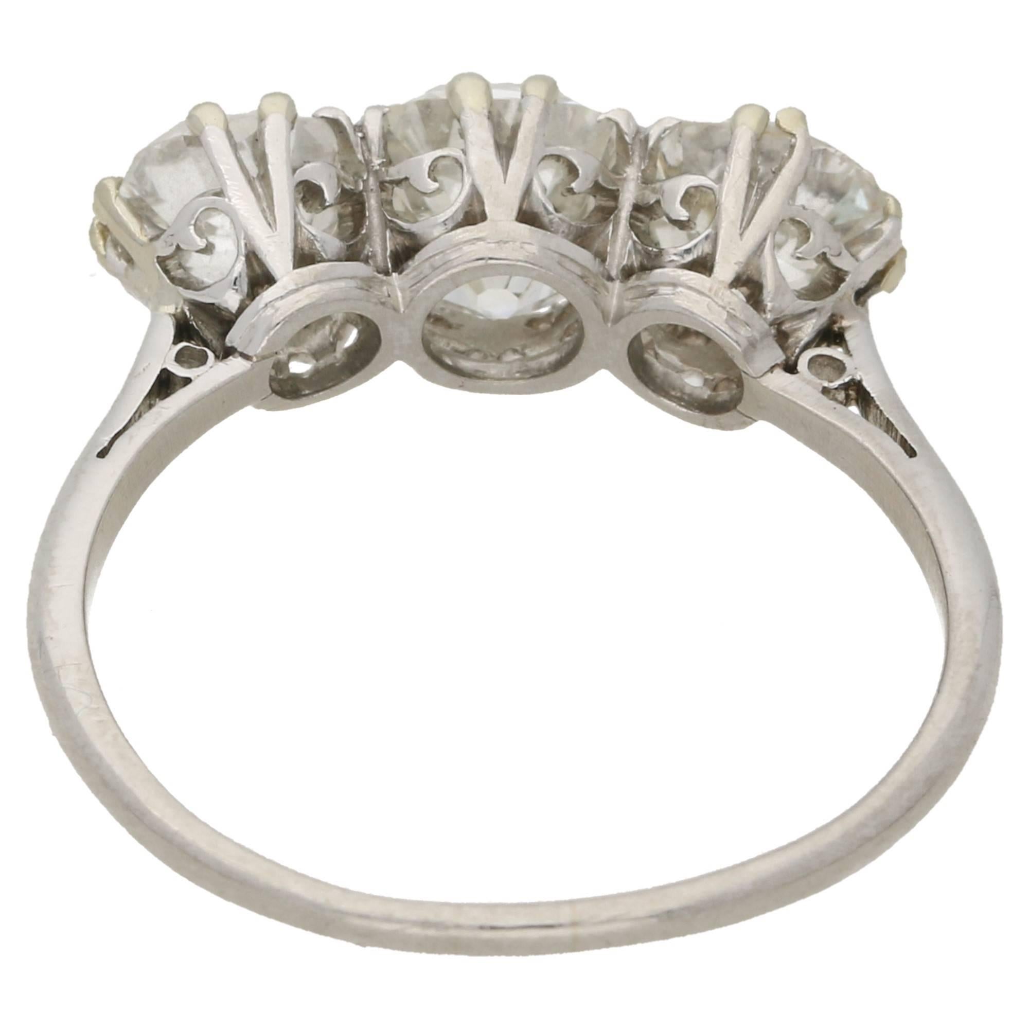 A stunning Edwardian three stone Old European cut diamond ring set in platinum. The Old European cut diamonds are split claw set, with stylised hearts adorning the undercarriage, embellished with open cheniers. Estimated total diamond weight: