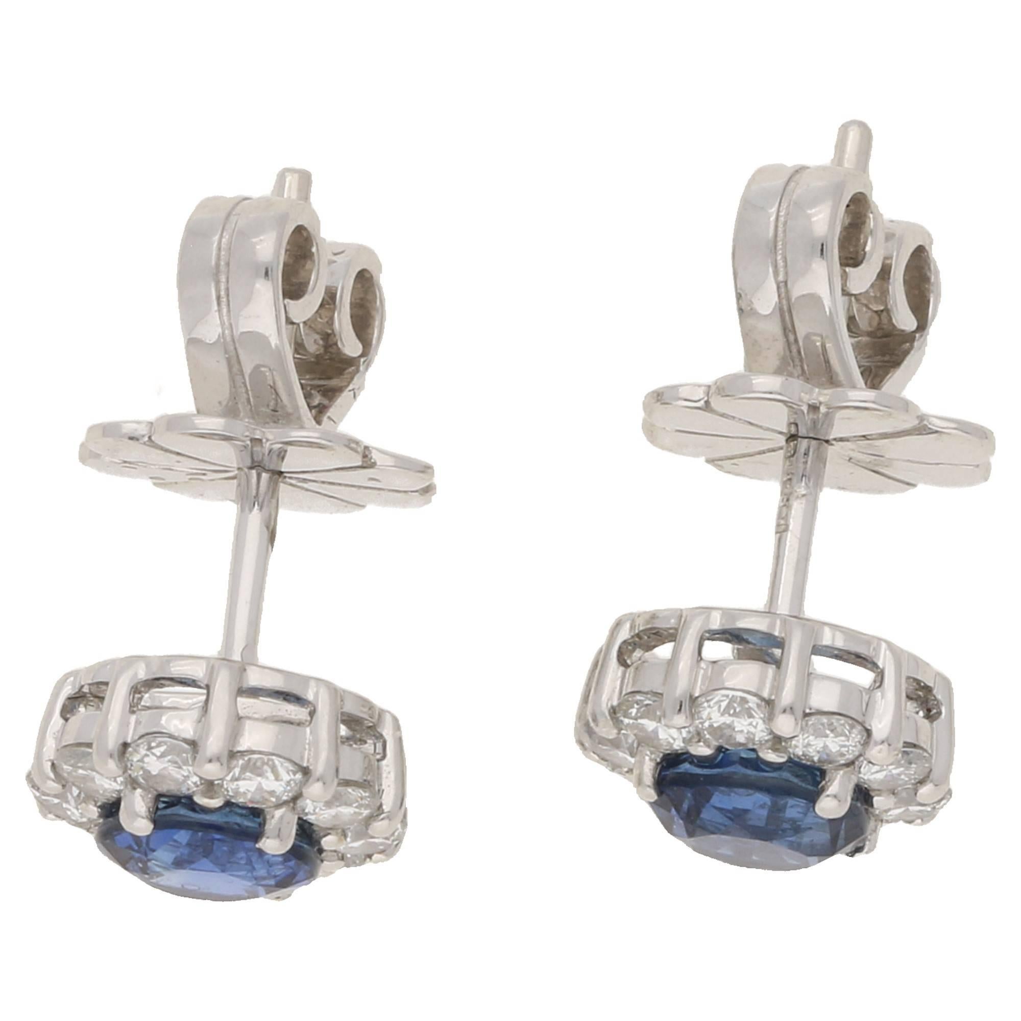 A fine pair of cluster earrings, set with central blue sapphires measuring 1.09cts total. The surrounding round brilliant cut diamonds total 0.76cts G/H colour and VS clarity, in a simple claw setting in 18k white gold. On post and butterfly