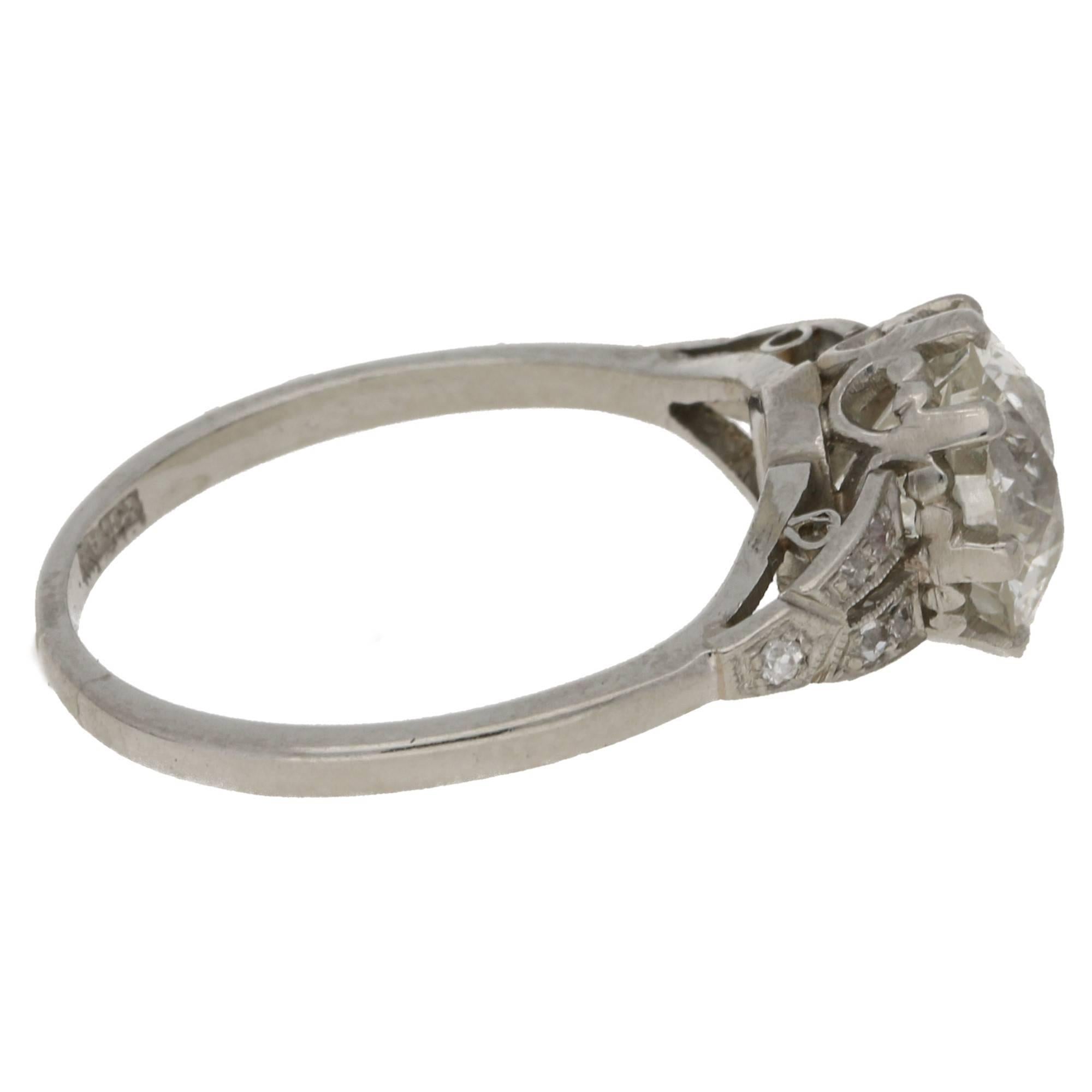 A very unique platinum single stone engagement ring featuring a K Si2 2.47ct Old European cut diamond in an eight claw setting with shield shaped shoulders. Each grain is set with five old cut diamonds to a straight 1.50mm width shank. The ring