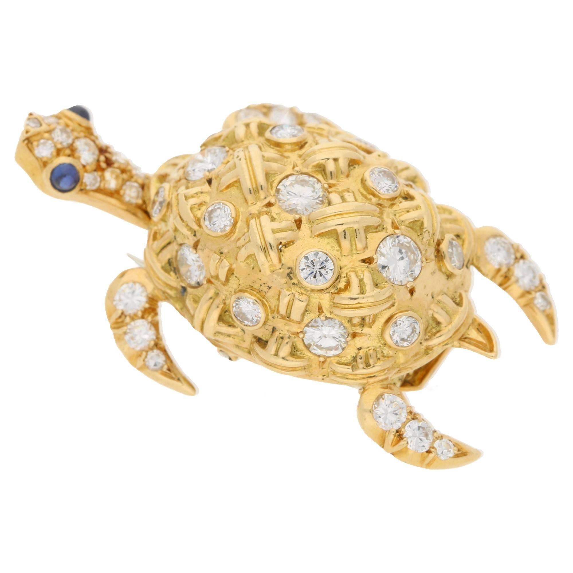 A diamond and gold brooch. The brooch is in the designed of a sea turtle with a brilliant-cut diamond and cross motif shell and round brilliant-cut diamond limbs, the articulated head is set with sapphires as eye details. Signed J.W. Estimated total