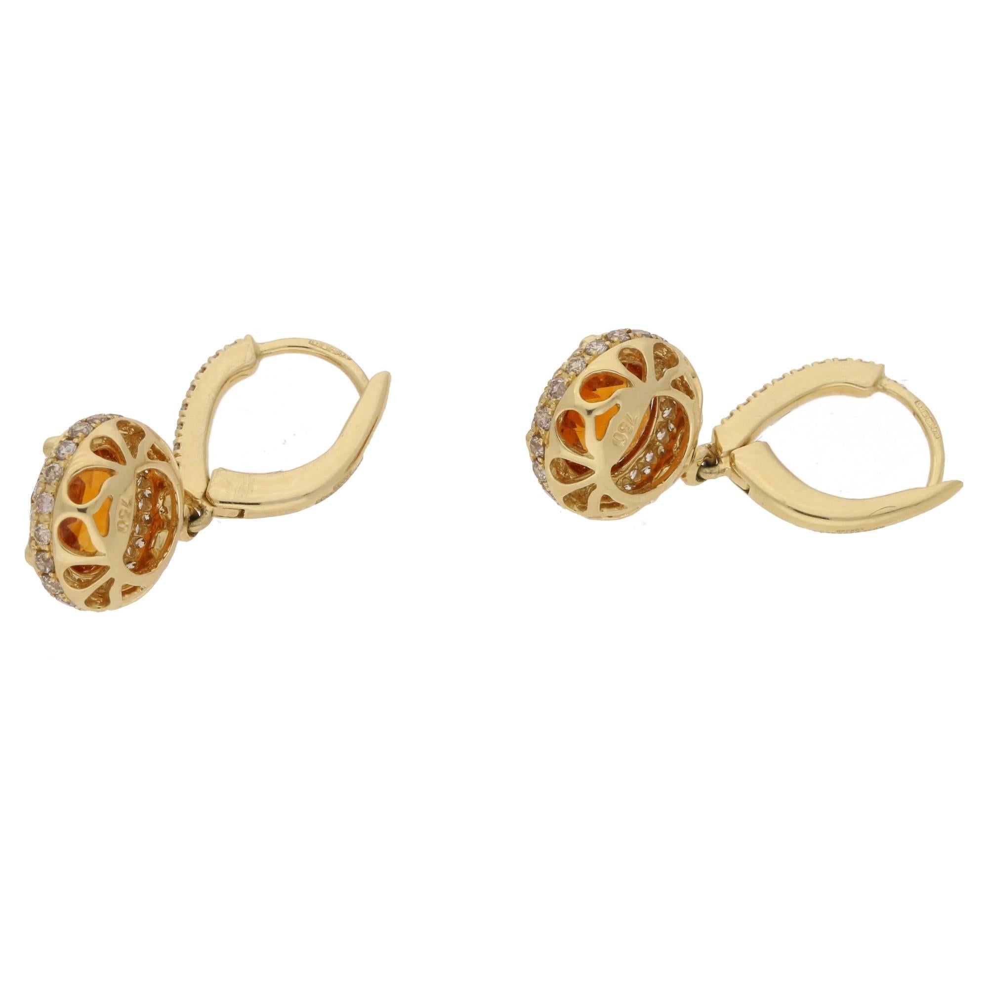 A vibrant pair of contemporary earrings, each set with a round central citrine, with intense orange colouring. The surround comprises of round brilliant diamonds of 0.29cts. On simple click closed hook fittings, in 18ct hallmarked gold.