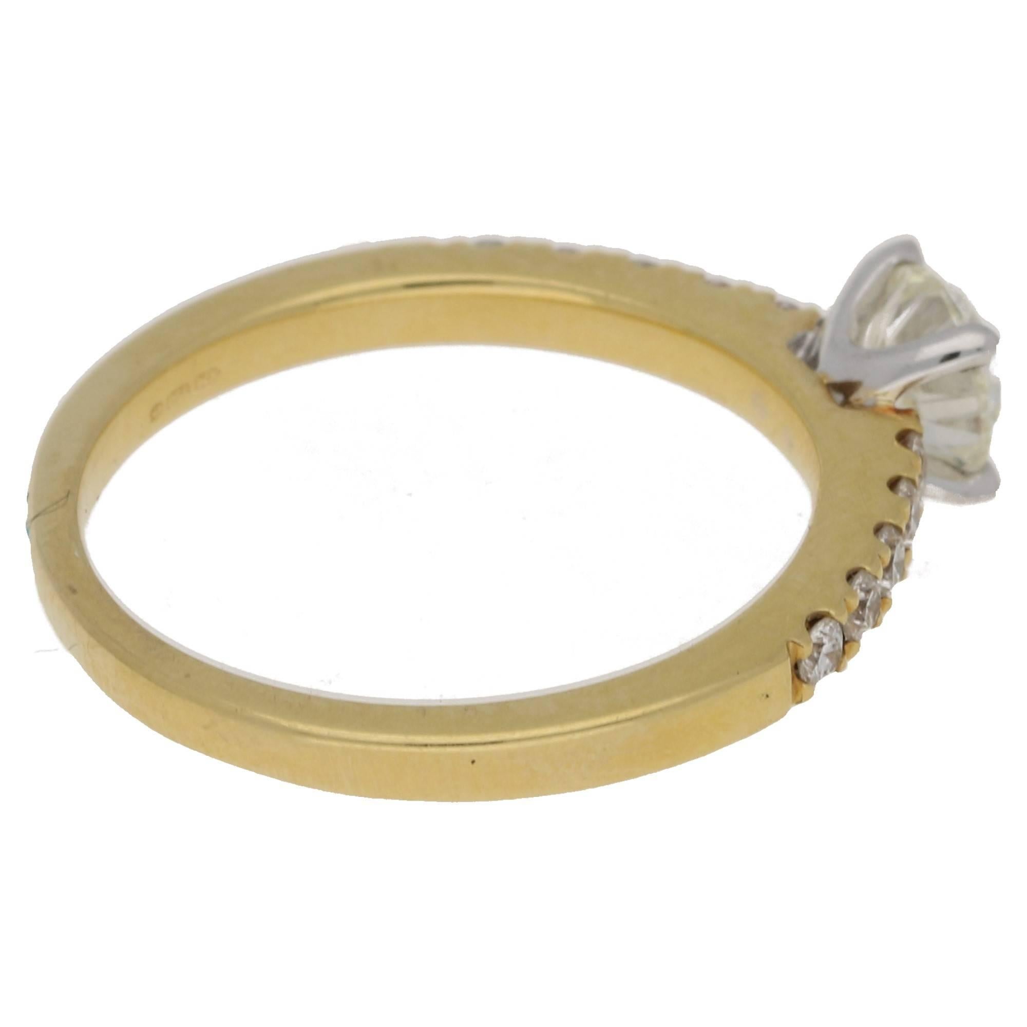 A contemporary diamond solitaire ring set in 18ct yellow and white gold. The centrally set round brilliant cut diamond is four claw set in 18ct white gold, and shouldered with ten brilliant cut diamonds grain set in 18ct yellow gold. Estimated