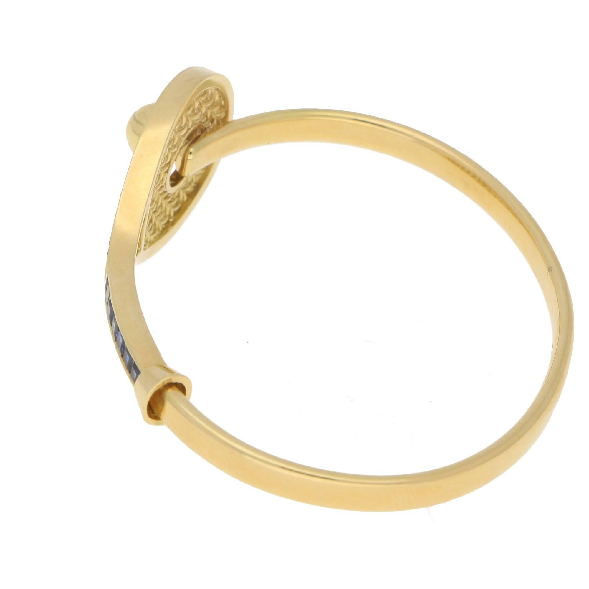 An amazing yellow gold hinged bangle. The bangle is fashioned as a tennis racket and ball. The racket is formed of a square sapphire set handle leading to a diamond set frame. The closing mechanism is cleverly designed featuring a solid gold tennis