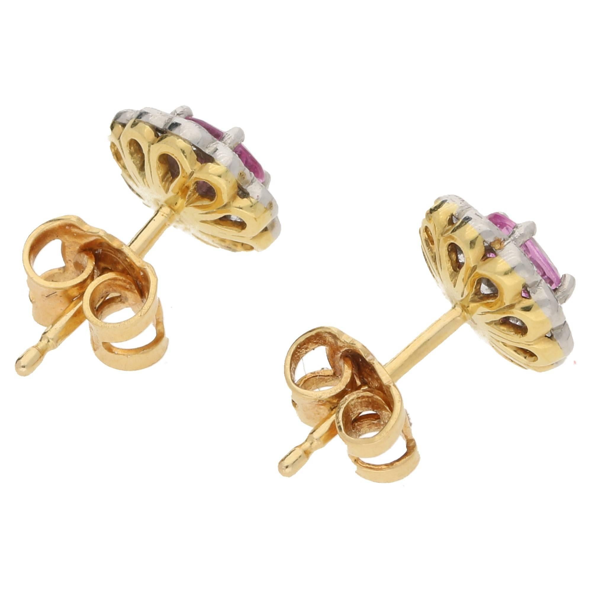 A fanciful pair of oval pink sapphire and diamond cluster ear studs set in 18ct white and yellow gold. The oval cut pink sapphire is four claw set within a border of ten round brilliant cut diamonds scallop set in mille grain edged 18ct white gold.