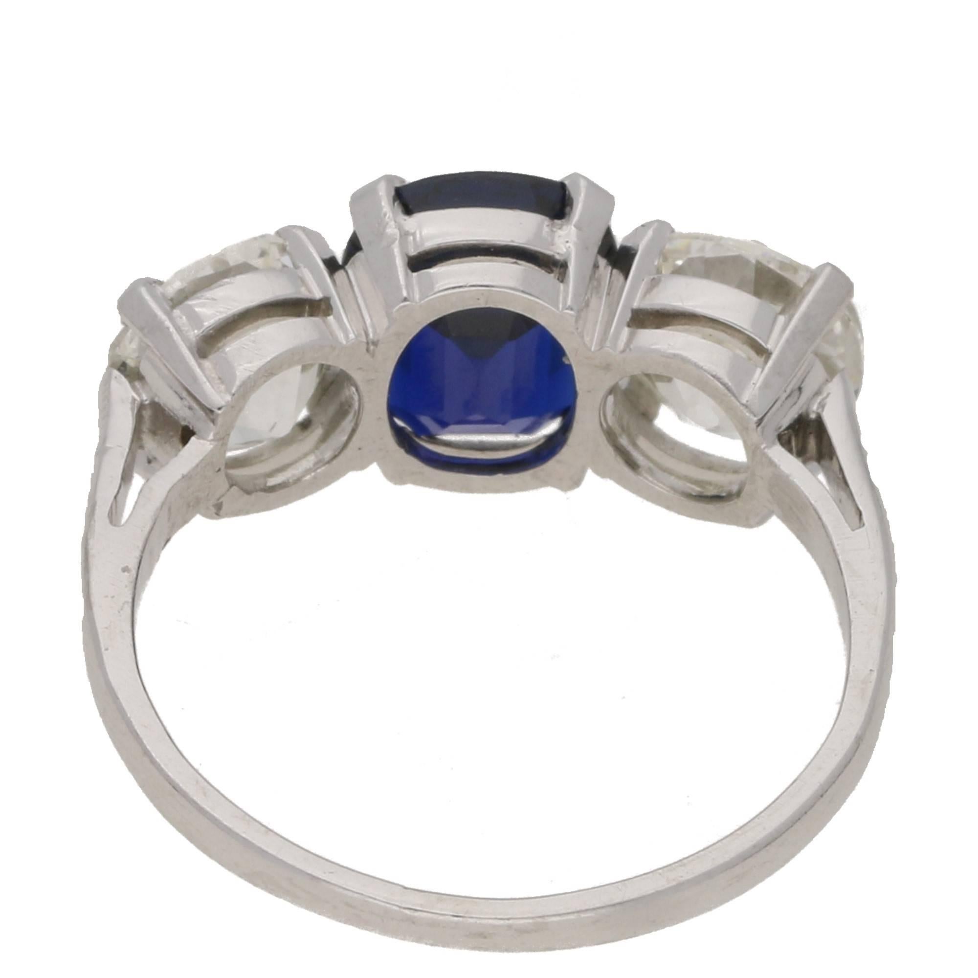 An exquisite three stone sapphire and diamond ring claw set in platinum. With a fantastic cushion-cut midnight blue velvet colour sapphire, set in a  four-claw double gallery setting. Shouldered with an immaculate pair of Old European cut diamonds.