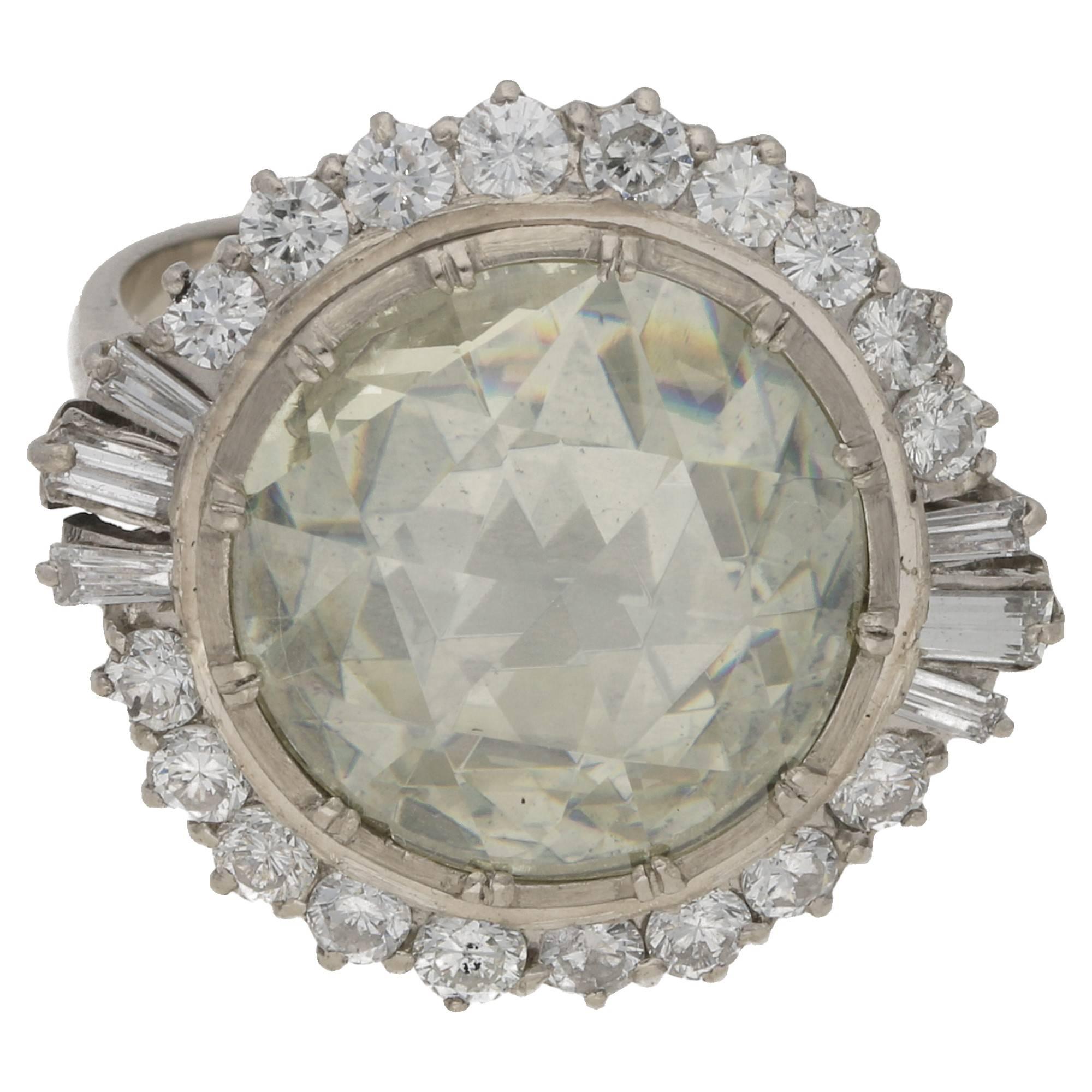 A significant rose cut Dimond cocktail ring. The ring is formed of a 4.66 carat rose cut diamond bezel set to the centre in a closed back setting. The principal stone is surrounded by a singular row of round brilliant cut diamonds peg set and
