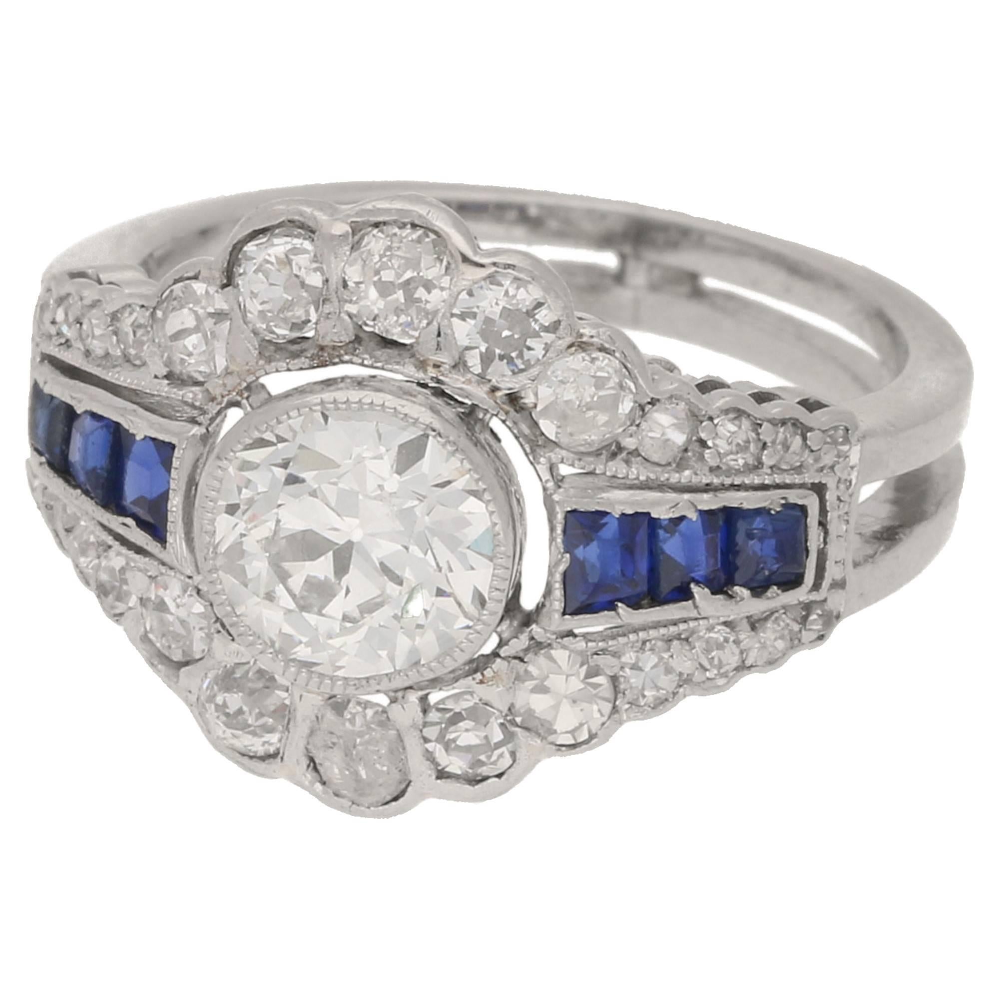  A platinum original Art Deco ring. Featuring an Old European cut diamond centre stone set in a rubover millegrain setting, with a pierced openwork geometric cluster comprising of old cut diamonds, and calibre cut sapphires in micro claw settings to