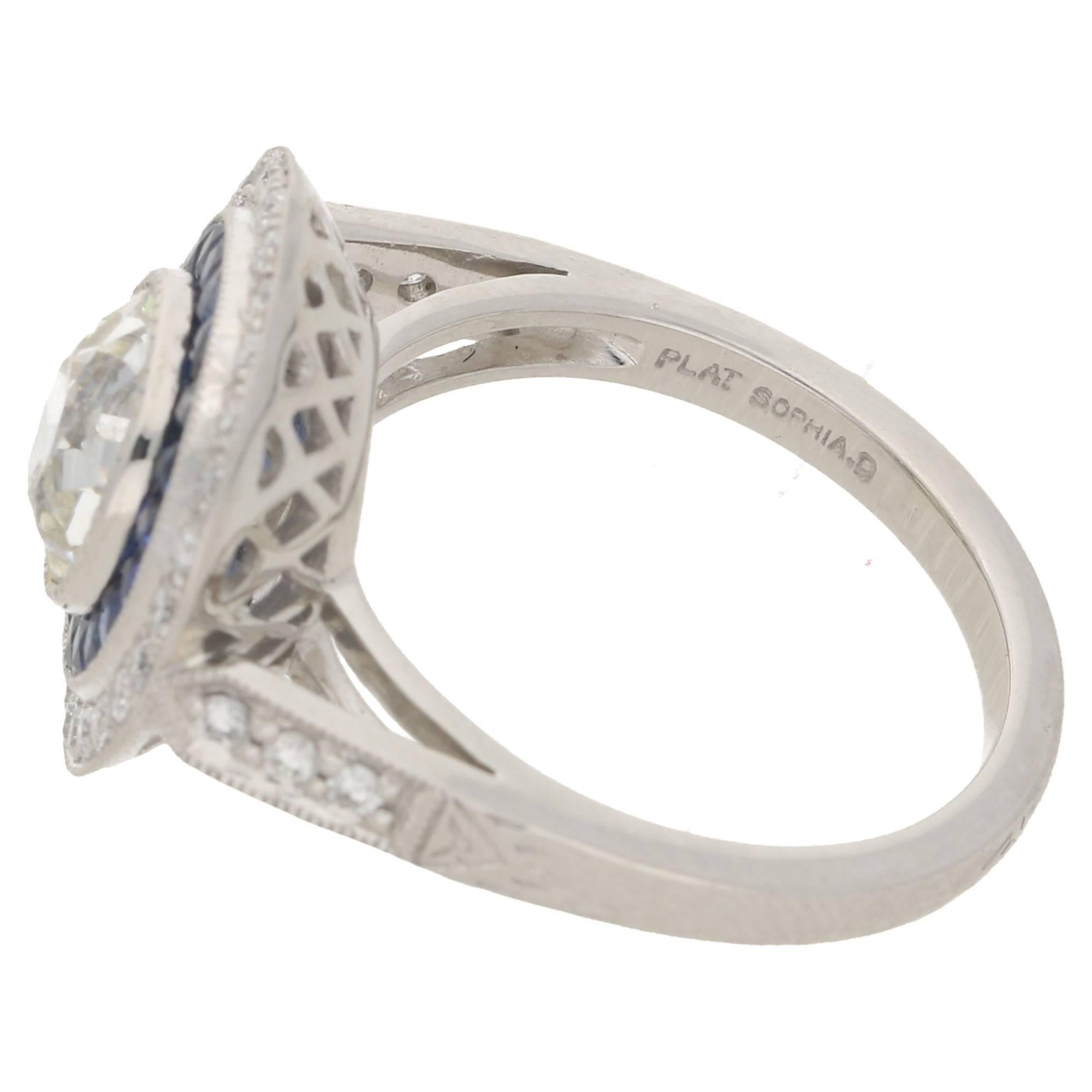 A platinum Art Deco design ring featuring an Old European cut diamond set in a rub over millegrain setting and estimated as 1.15 carats, I/J colour and Si clarity, surrounded by a halo of French cut sapphires with an estimated weight of 0.67 carats