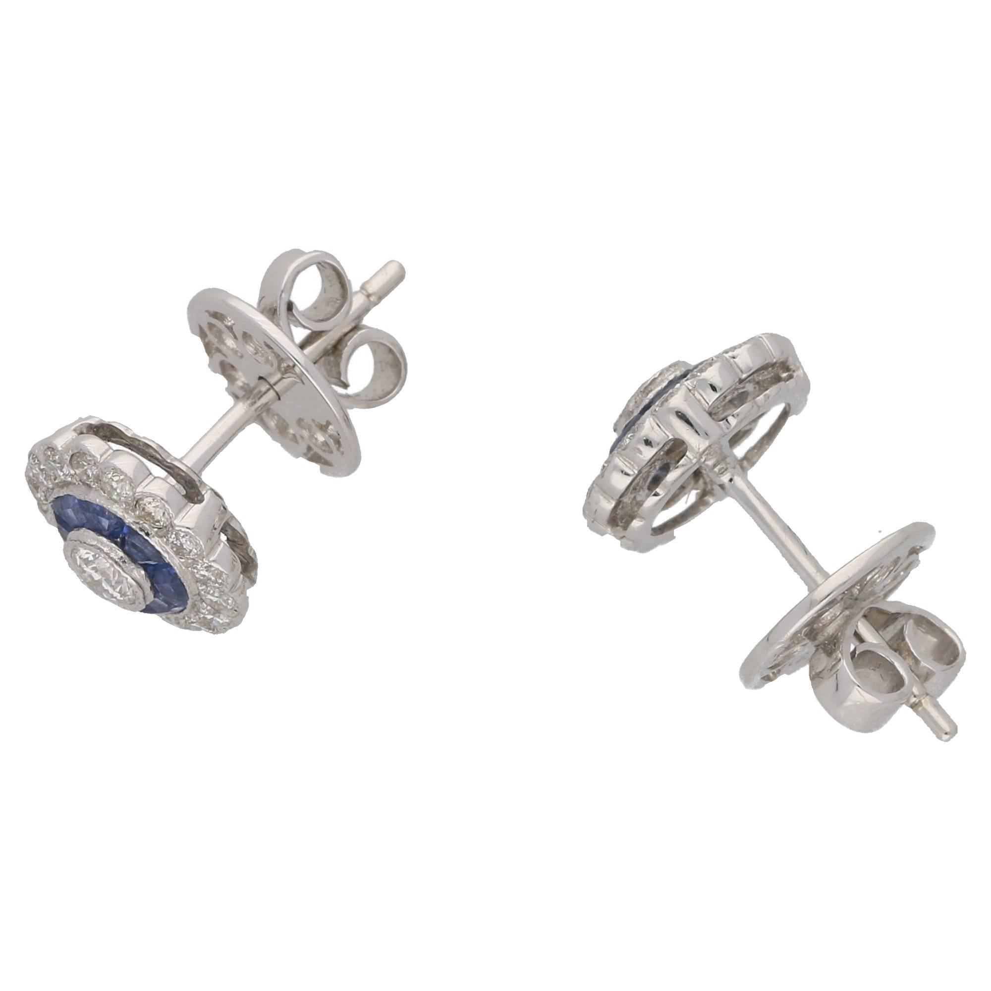 A wonderful pair of sapphire and diamond 18ct white gold stud earrings. Each earring consists of a centrally set round brilliant cut diamond collet set in mille grain 18ct white gold. The diamond is encased in a surround of calibre cut channel set