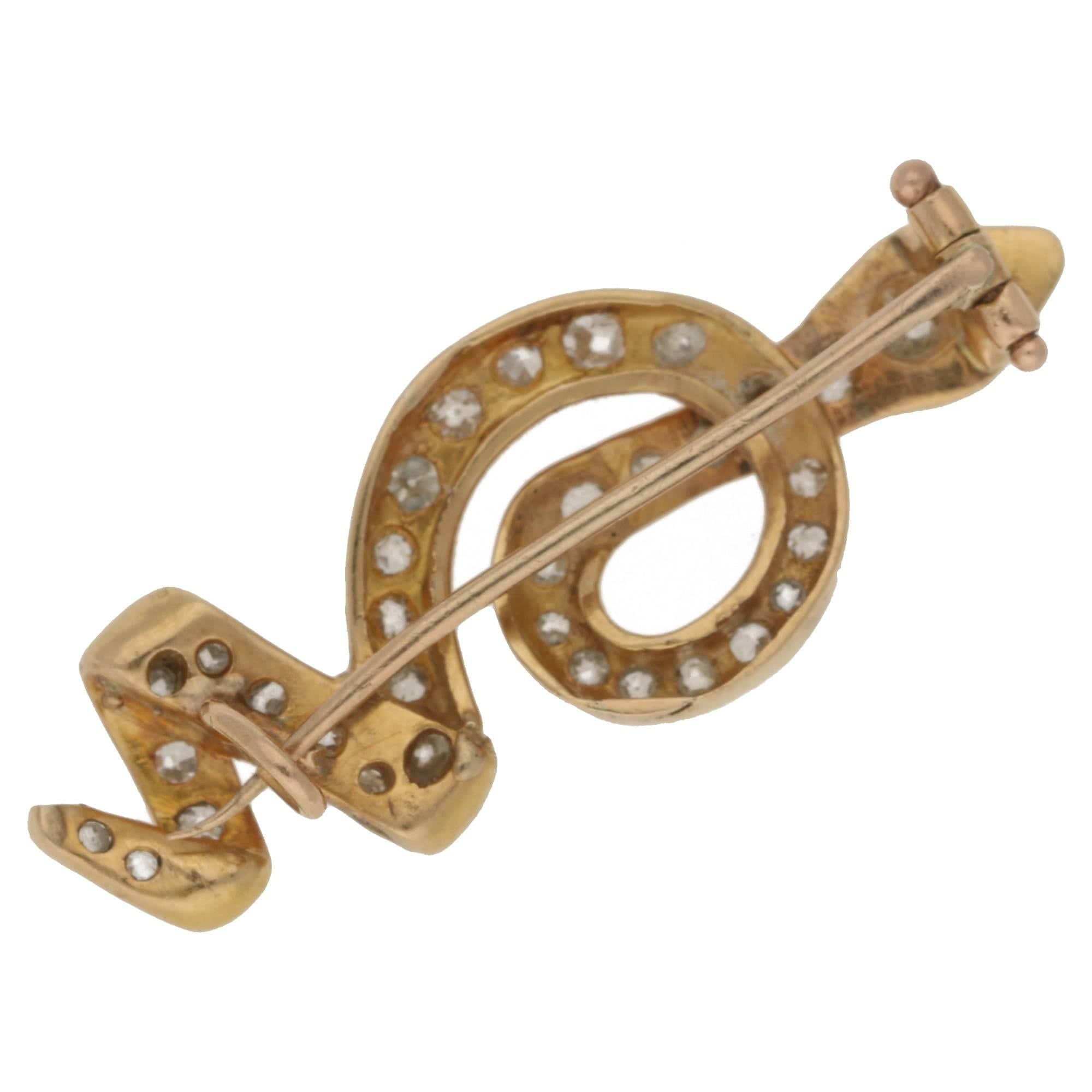 A mid-20th century snake brooch in 18ct yellow gold grain set with thirty-three Old European cut diamonds and ruby eyes, in a squiggle design. The brooch measure 38.50mm in length and 15.00mm in width and has a trombone pin fastening to a C-catch