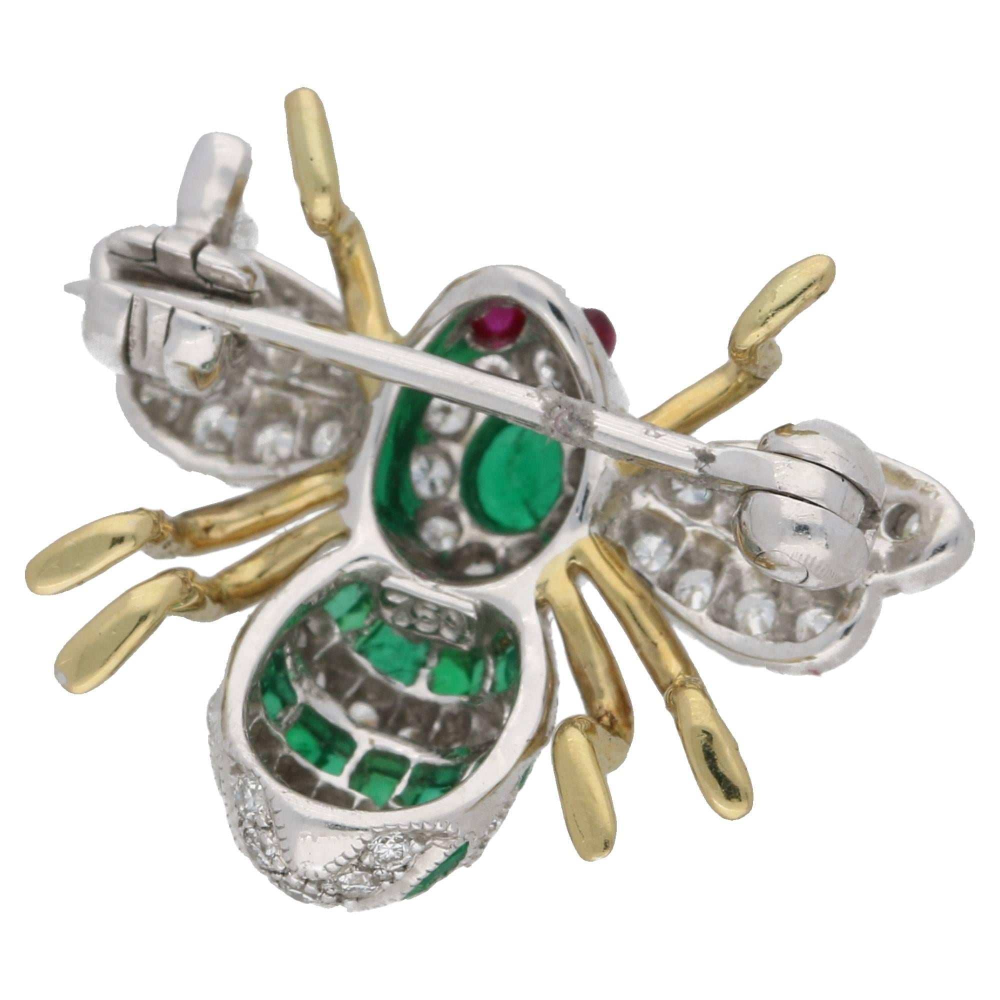 A beautifully crafted diamond and emerald bee brooch set in 18ct yellow and white gold. With cabochon ruby eyes, pave-set round brilliant cut diamond wings, and stripes of calibre-cut channel-set emeralds and lines of pave set diamonds adorning the