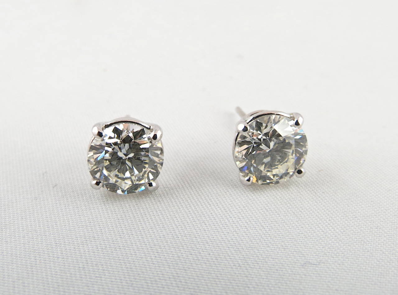 Round brilliant cut diamond stud earrings, showcasing a pair of meticulously matched brilliant cut diamonds weighing 5.00 total carats, the diamonds secured in classic four prong 18K white gold settings with posts and friction backs for pierced